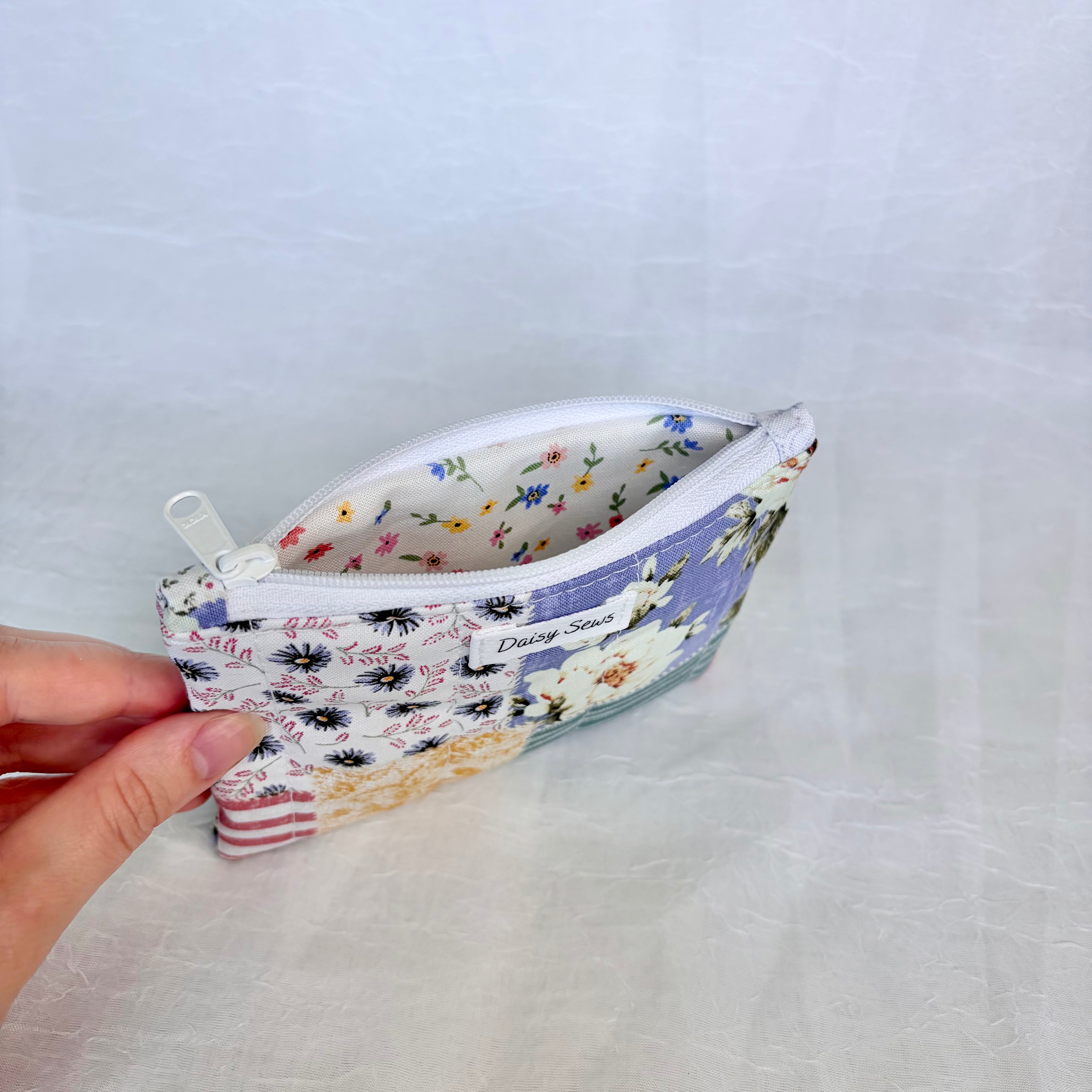 Small fabric pouch with floral pattern held by a hand on a light gray background