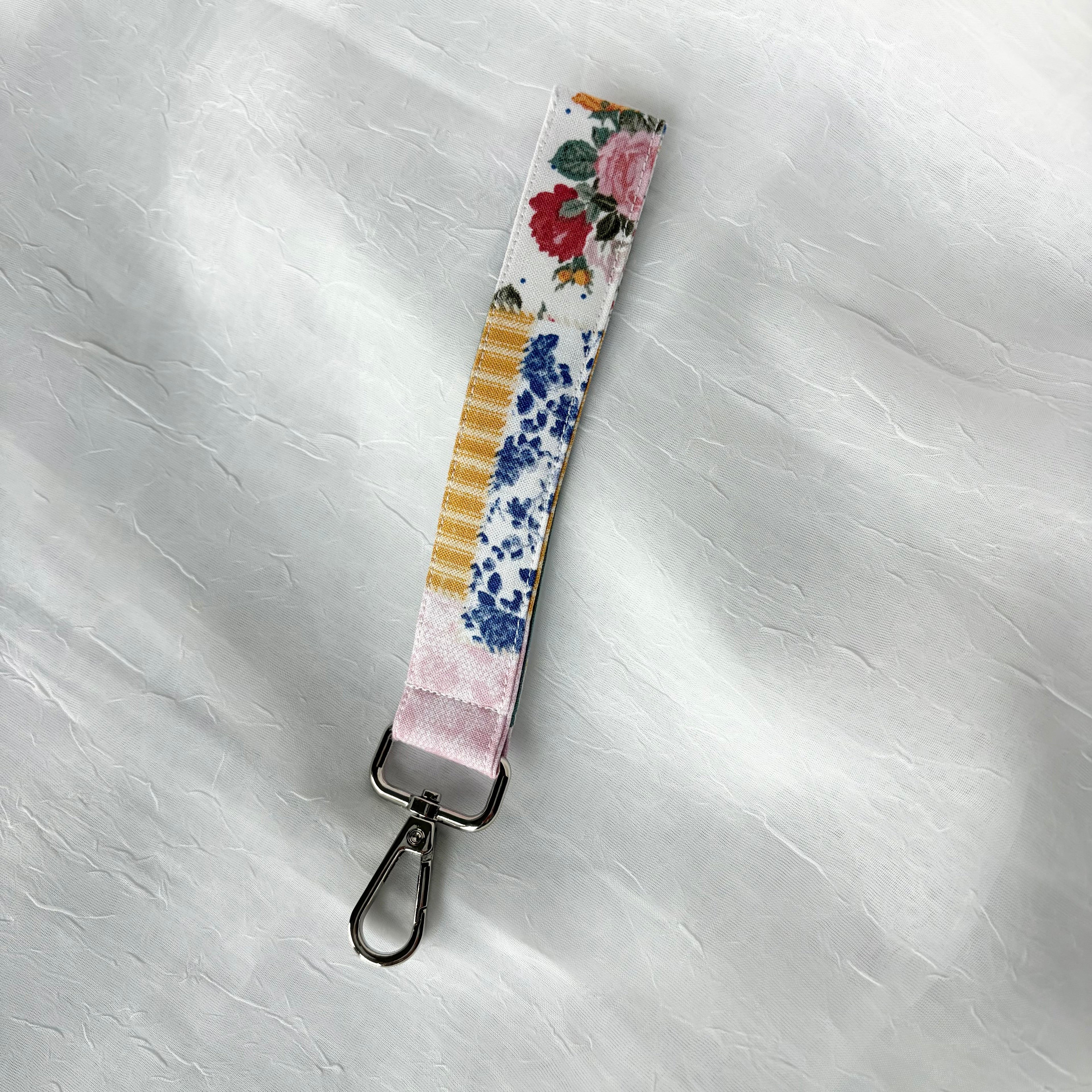 Colorful patchwork fabric keychain wristlet with silver lobster clip including yellow and white stripes, blue florals, and pink and red flowers.
