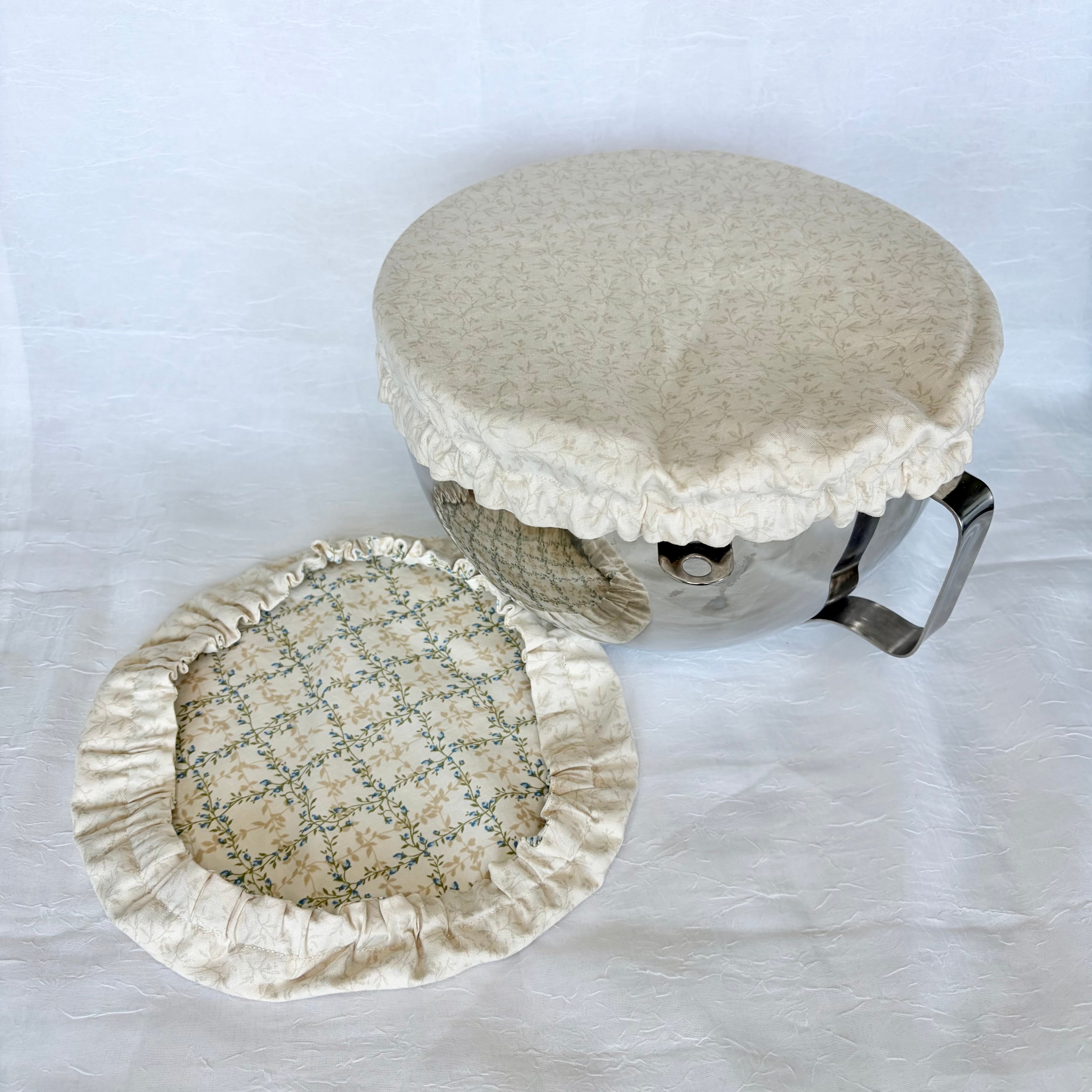cream floral cover on silver bowl with second blue, green and cream cover next to it