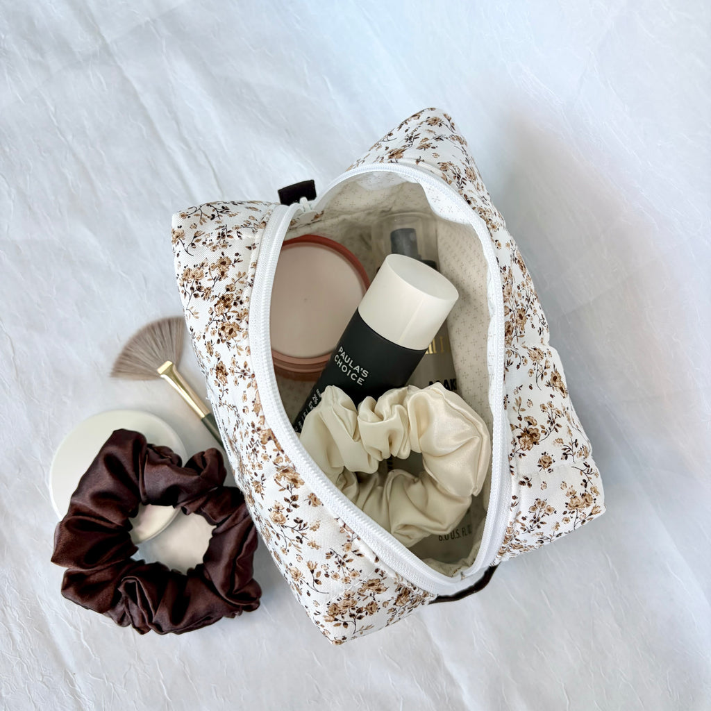 brown Floral-patterned makeup bag with beauty products and a scrunchie on a white background