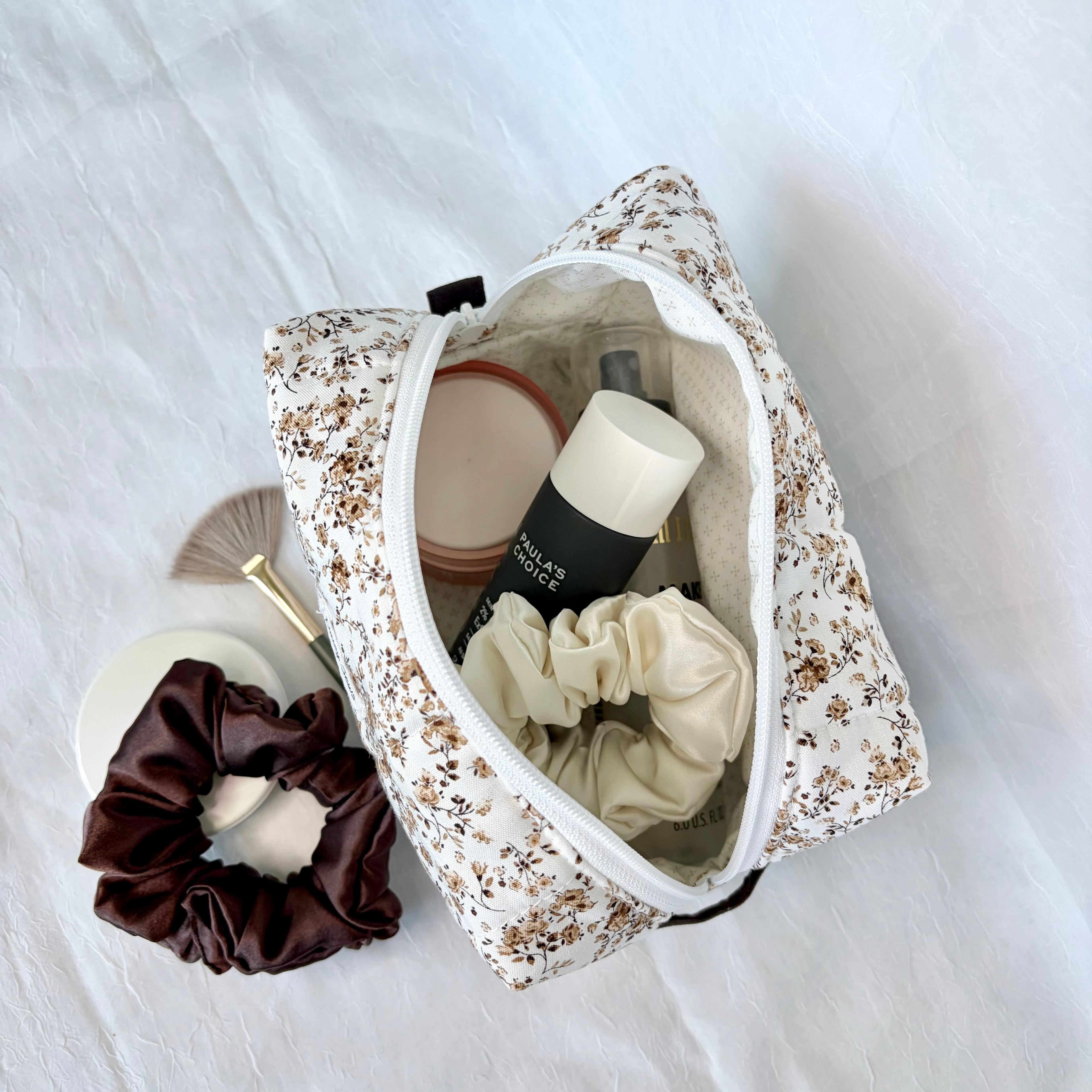 brown Floral-patterned makeup bag with beauty products and a scrunchie on a white background