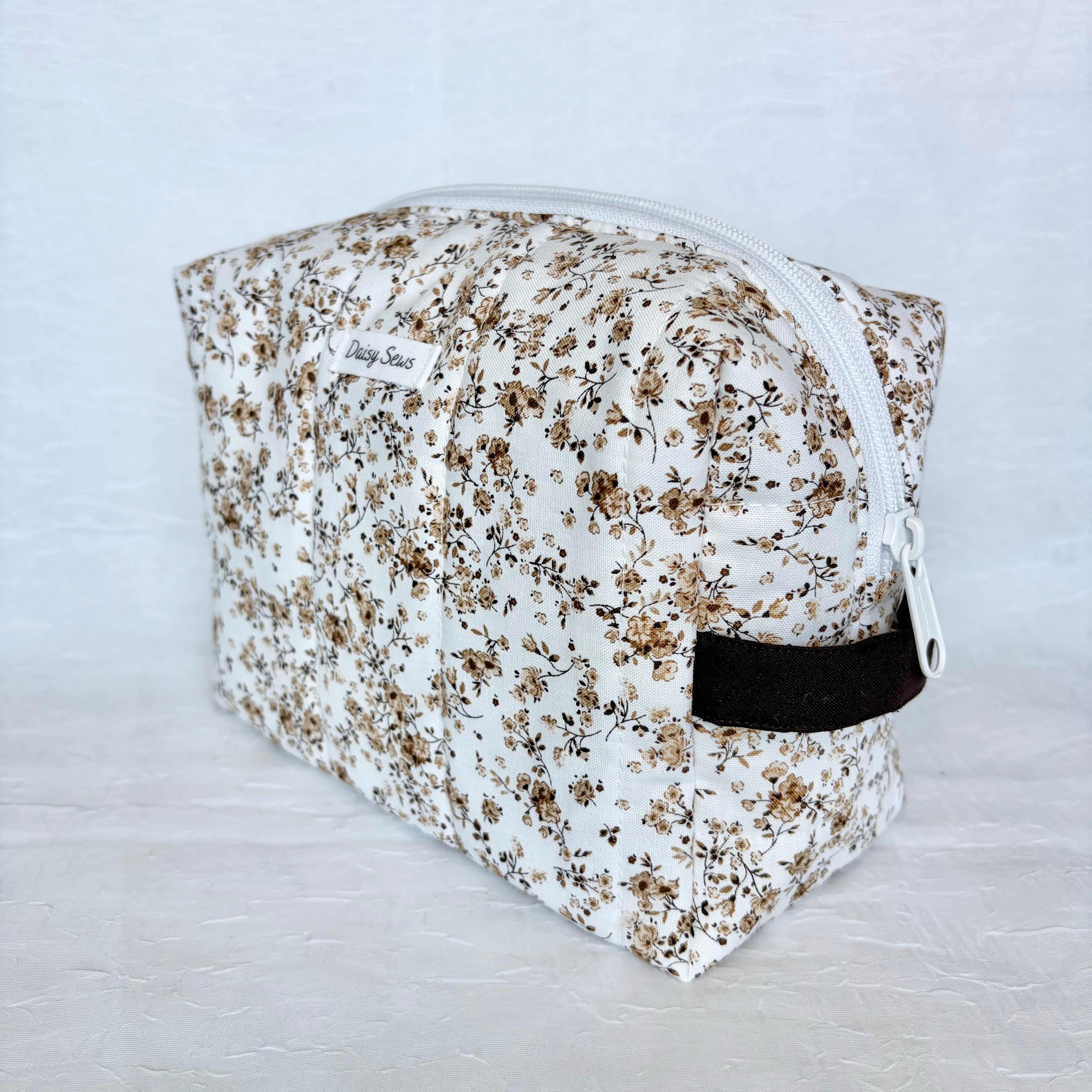 brown Floral-patterned makeup bag with a white zipper and brown handle on a light gray background