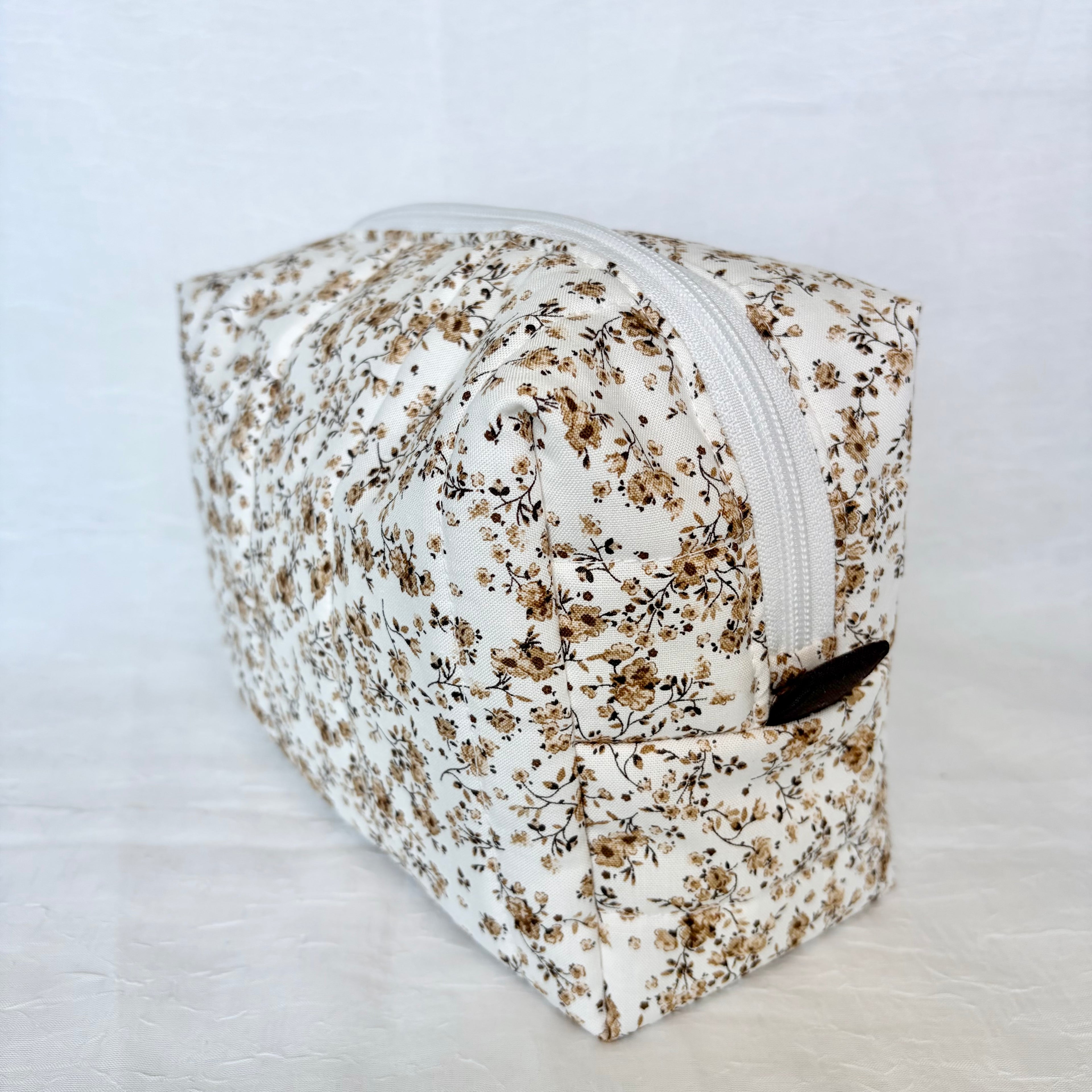 brown Floral-patterned toiletry bag with brown tab and white zipper on a light gray background