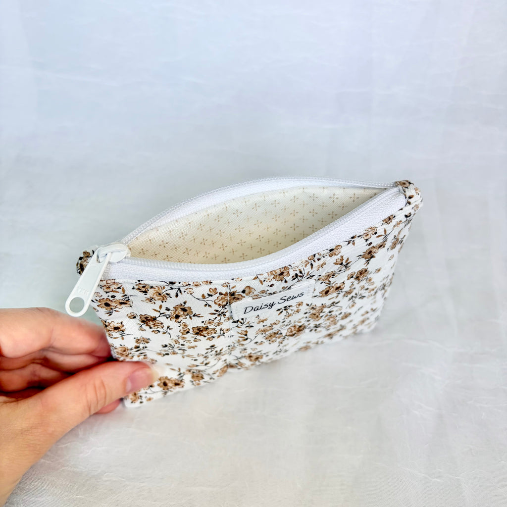 brown Floral-patterned pouch with cream liner held by a hand on a light gray background