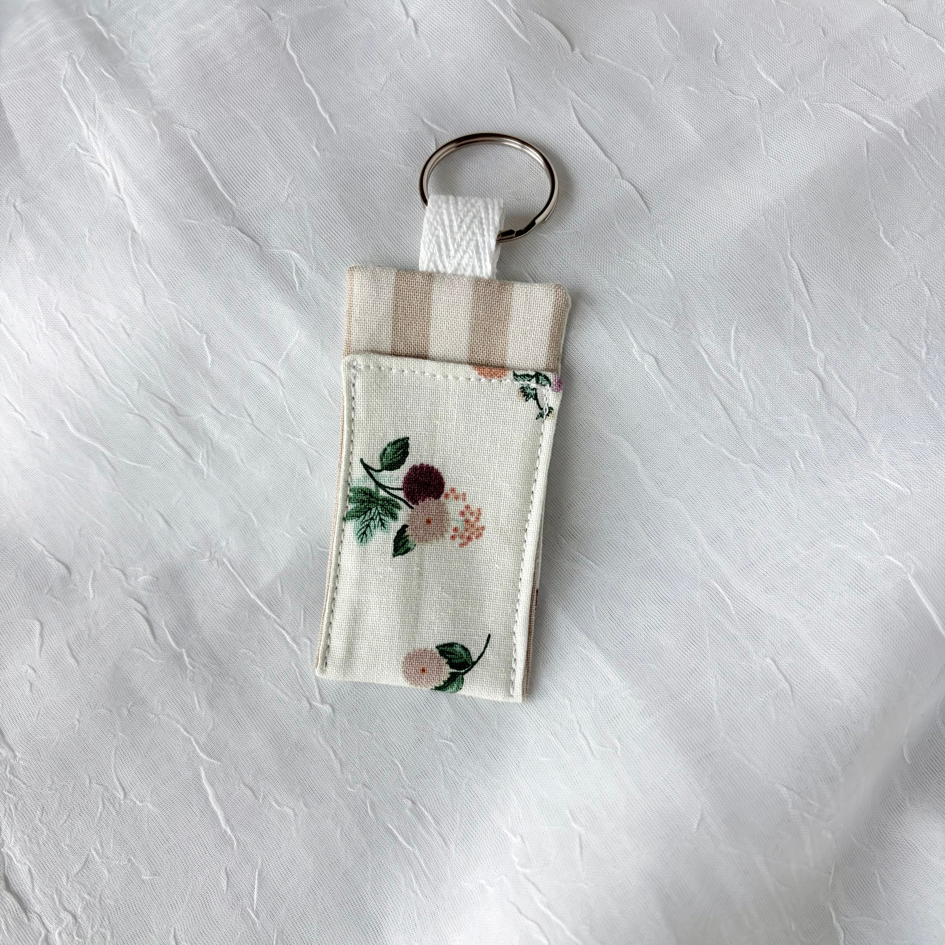Floral  on cream with tan strip liner chapstick holder with keychain ring on a textured white background