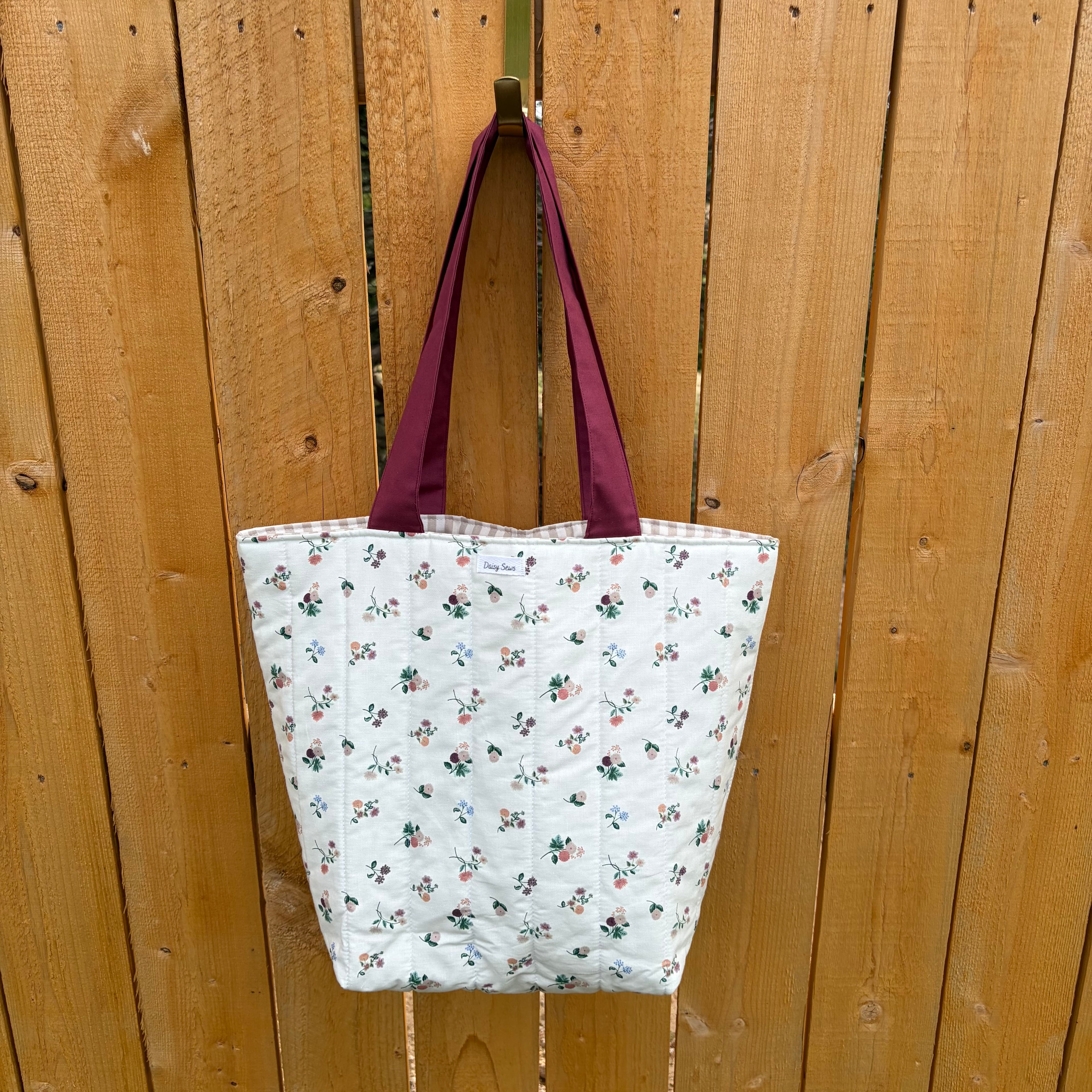 Floral on cream Tote Bag with maroon handles hanging on wooden fence