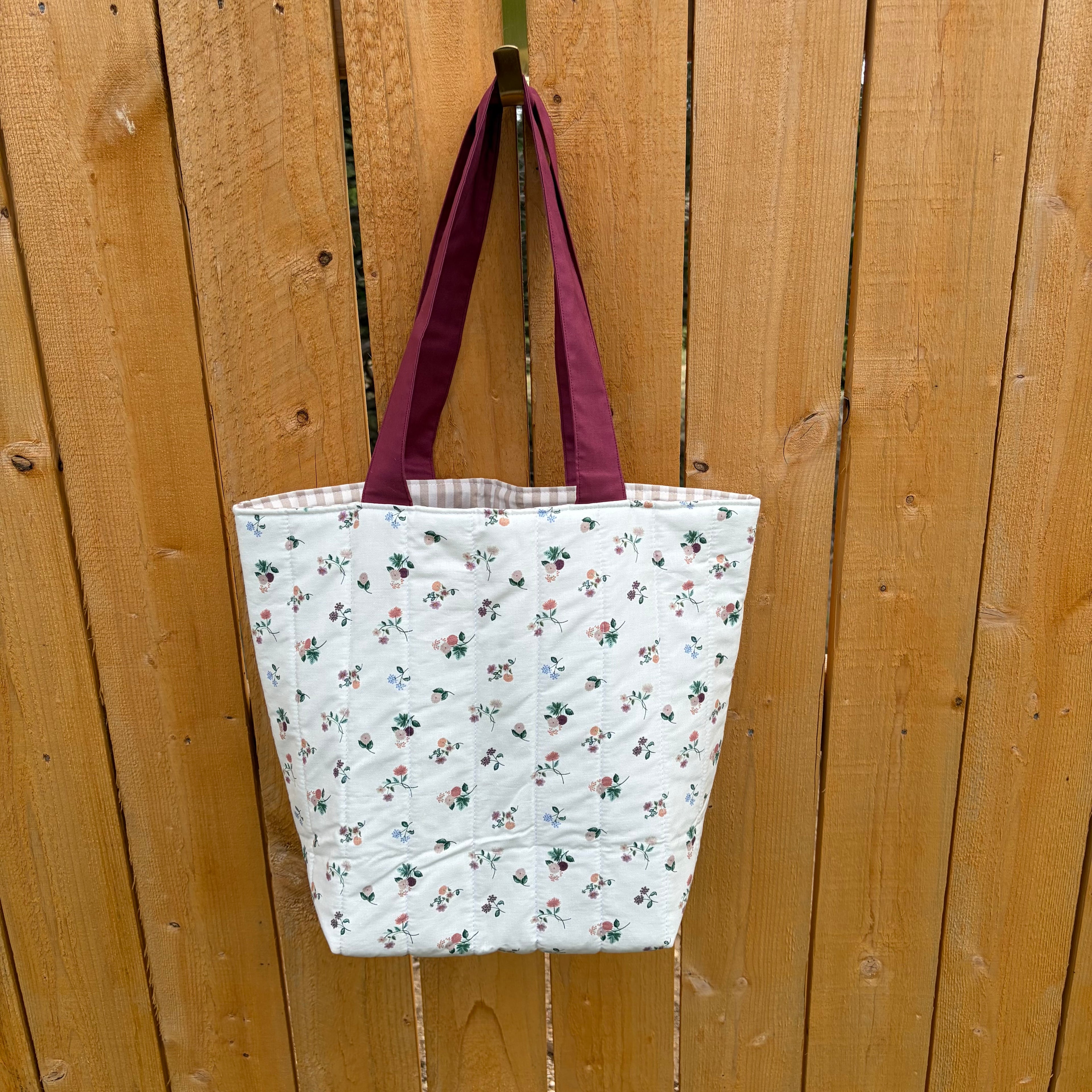 Back View Floral on cream Tote Bag with maroon handles hanging on wooden fence