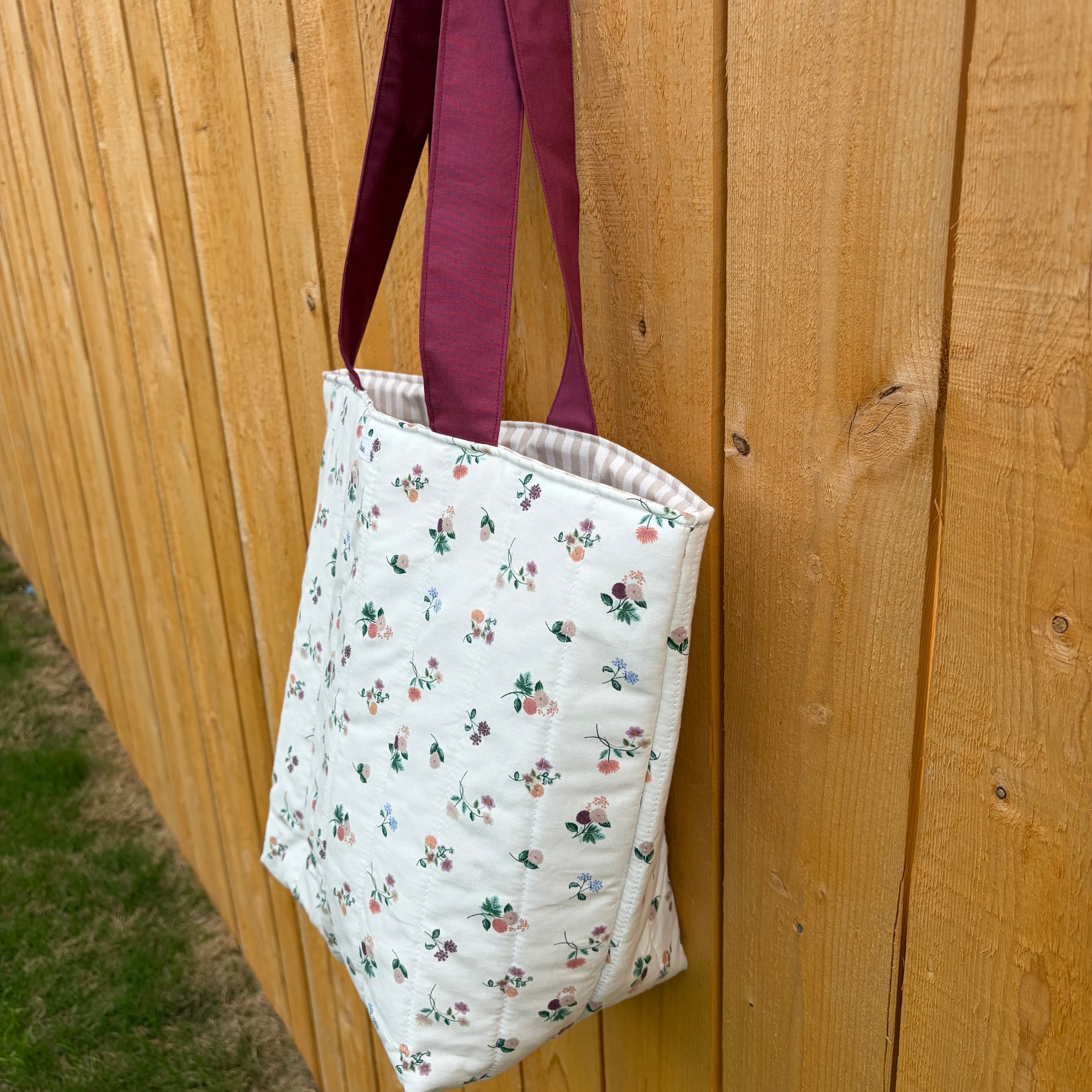 Side View Floral on cream Tote Bag with maroon handles hanging on wooden fence