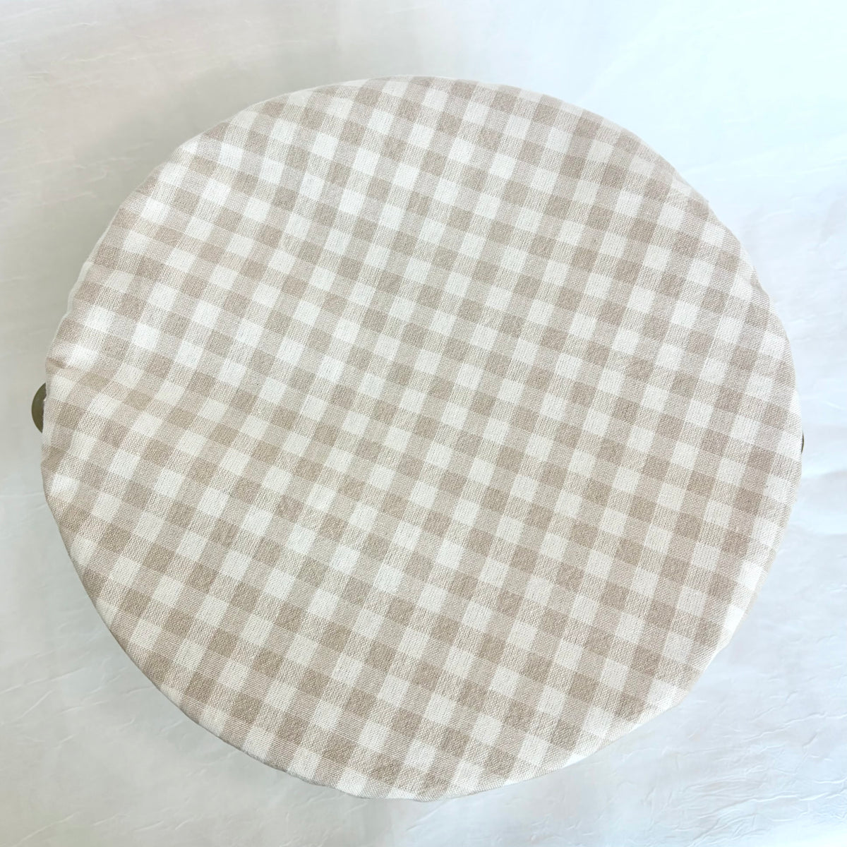 A round fabric-covered bowl with a beige and white gingham checkered pattern, photographed from above on a light background.