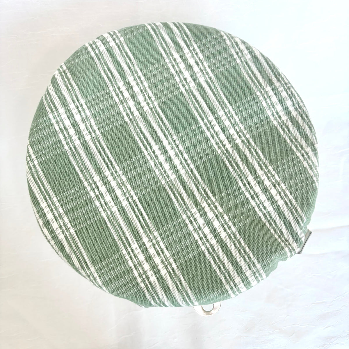 A round fabric-covered bowl with a green and white plaid pattern, photographed from above on a white fabric background.