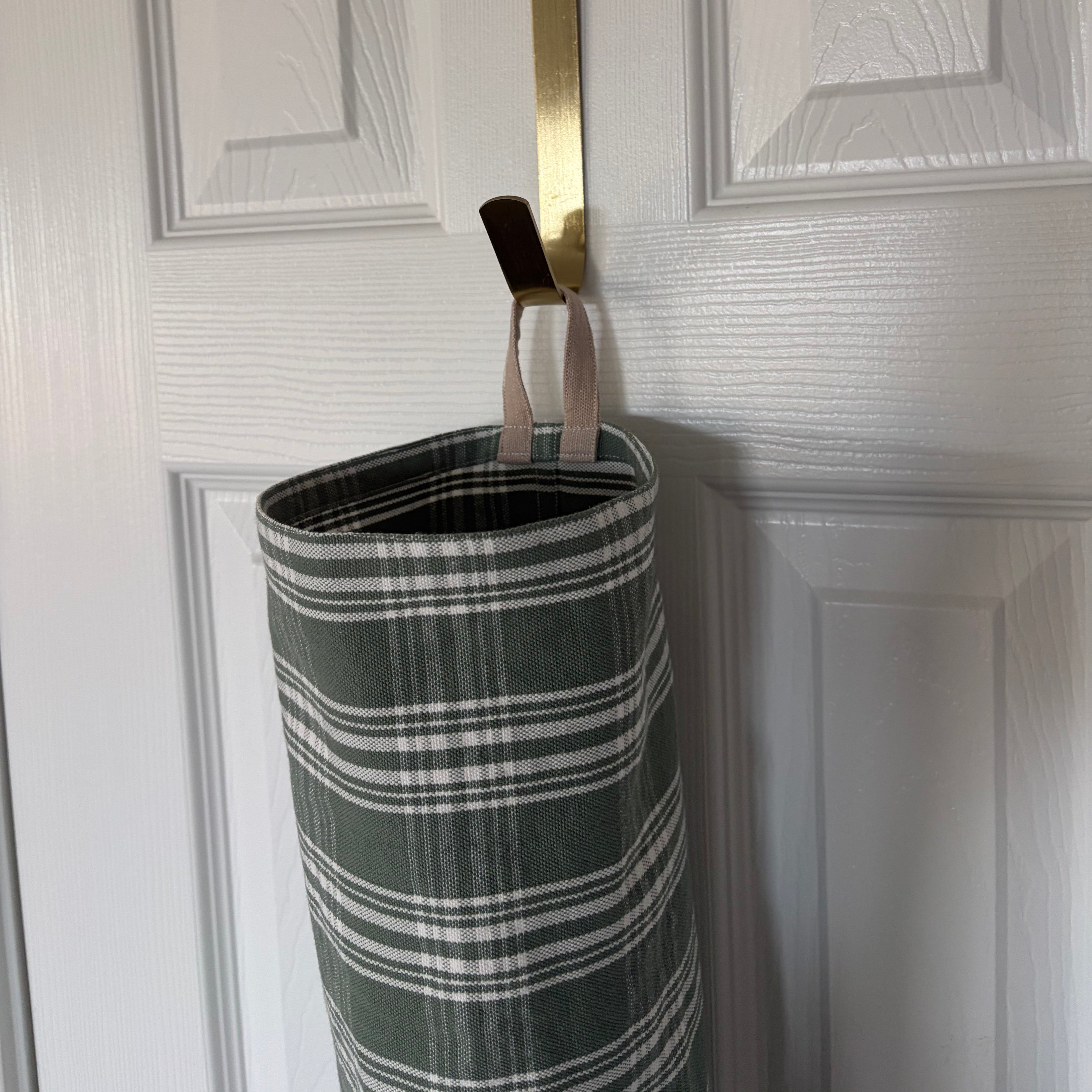  top view of hook holding the bag over a door. fabric in cylindrical shape with tan hook at the top and elastic on the bottom