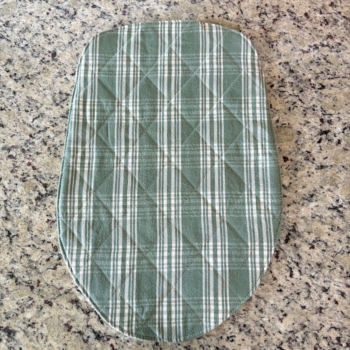 A quilted fabric mat, featuring a green and white plaid pattern, laid flat on a speckled granite countertop. head tilt size