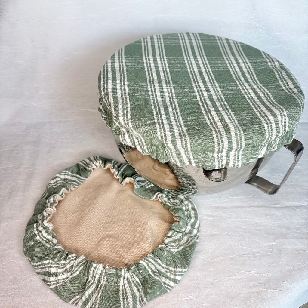 Green with white plaid bowl cover displayed on a metal bowl with a handle and a matching cover with tan interior on a light gray background