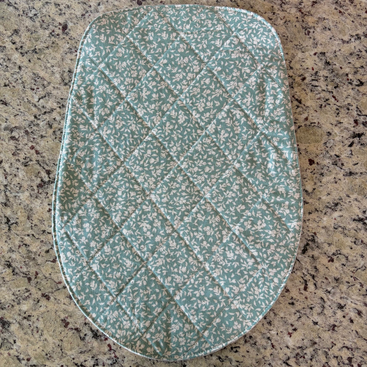 A quilted fabric pad with a small floral pattern in sage green and white, laid flat on a speckled granite countertop. head tilt size