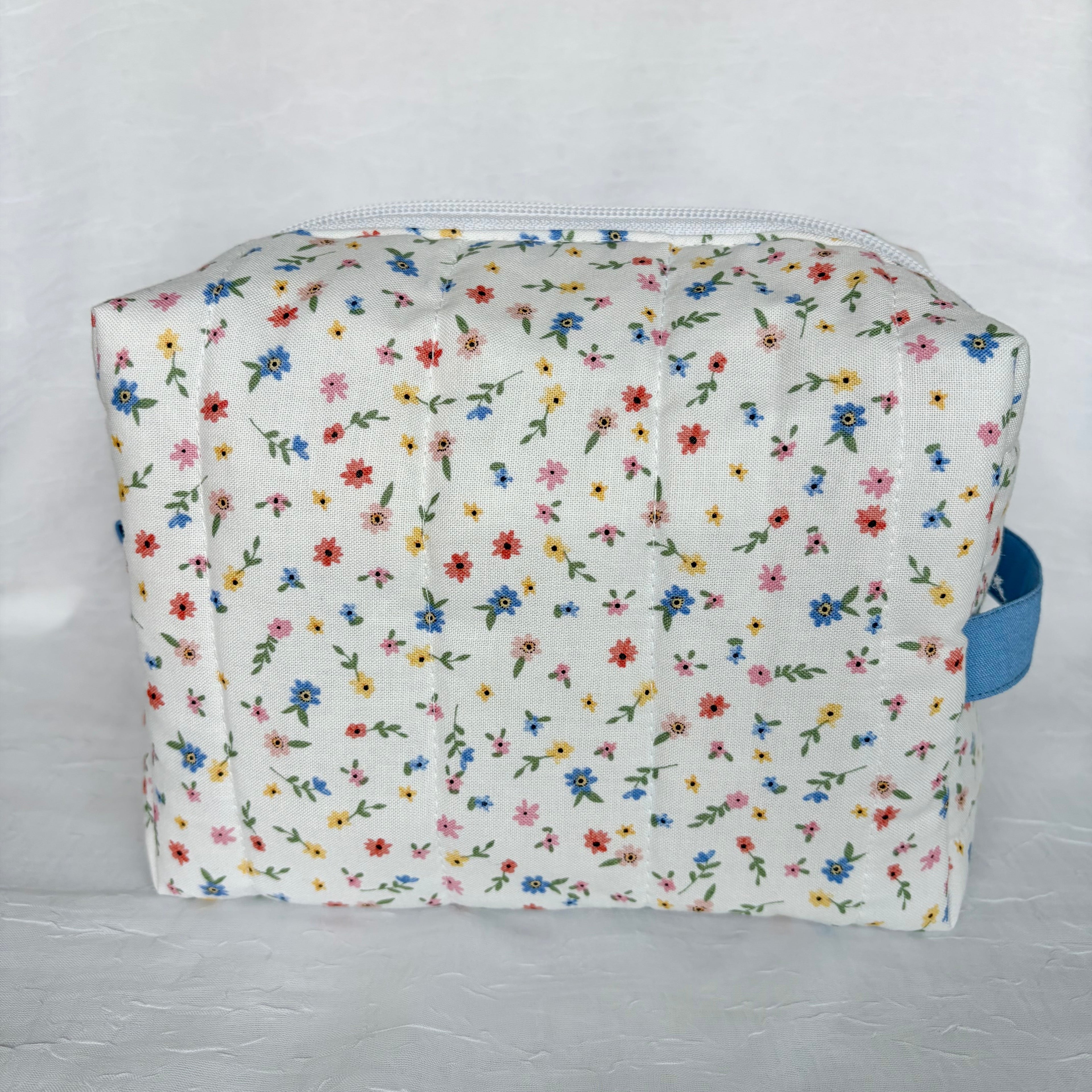 back view of little blue, yellow, pink and red flowers with green leaf patterned boxy bag on white background