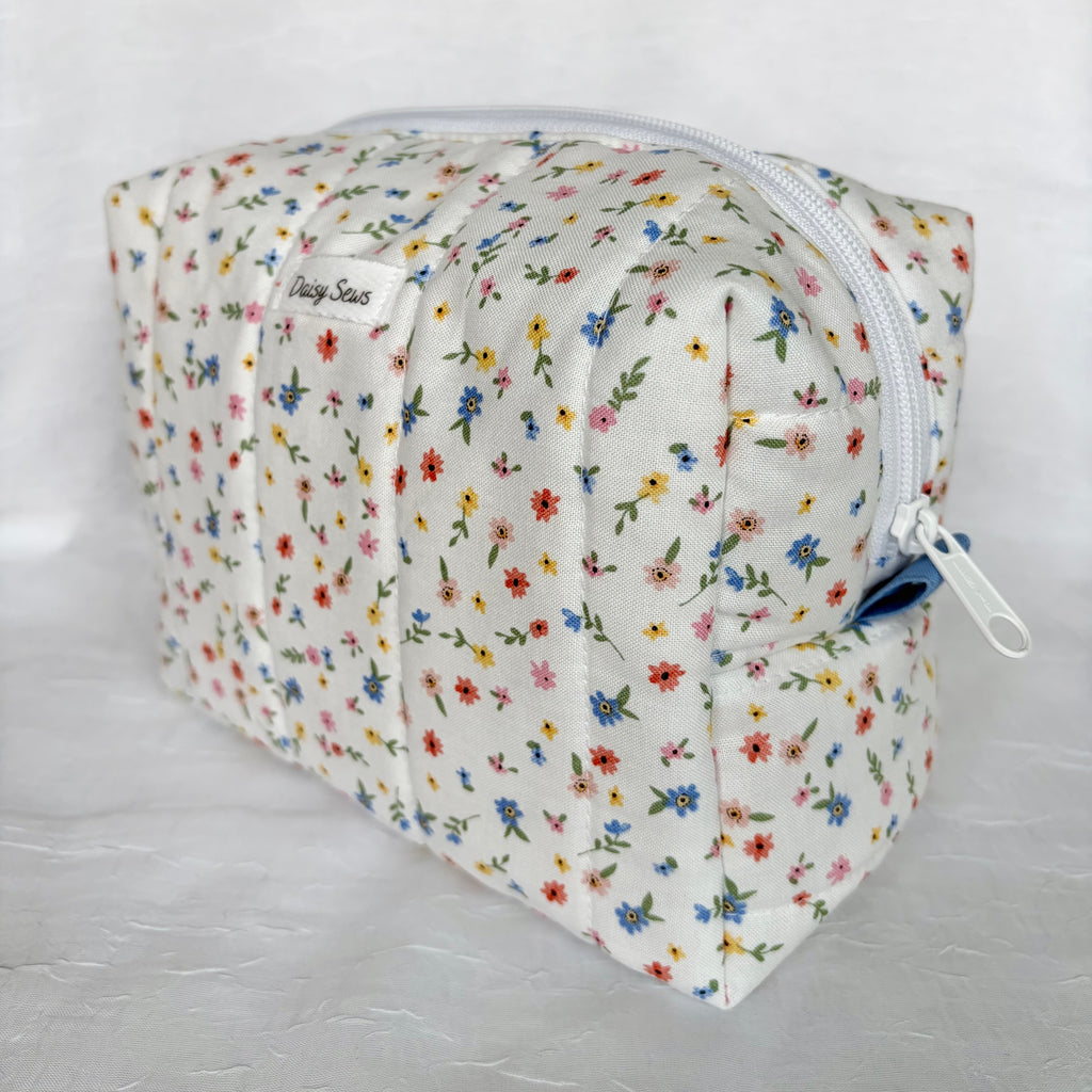 side view blue pull tab and white zipper on little blue, yellow, pink and red flowers with green leaf patterned boxy bag on white background