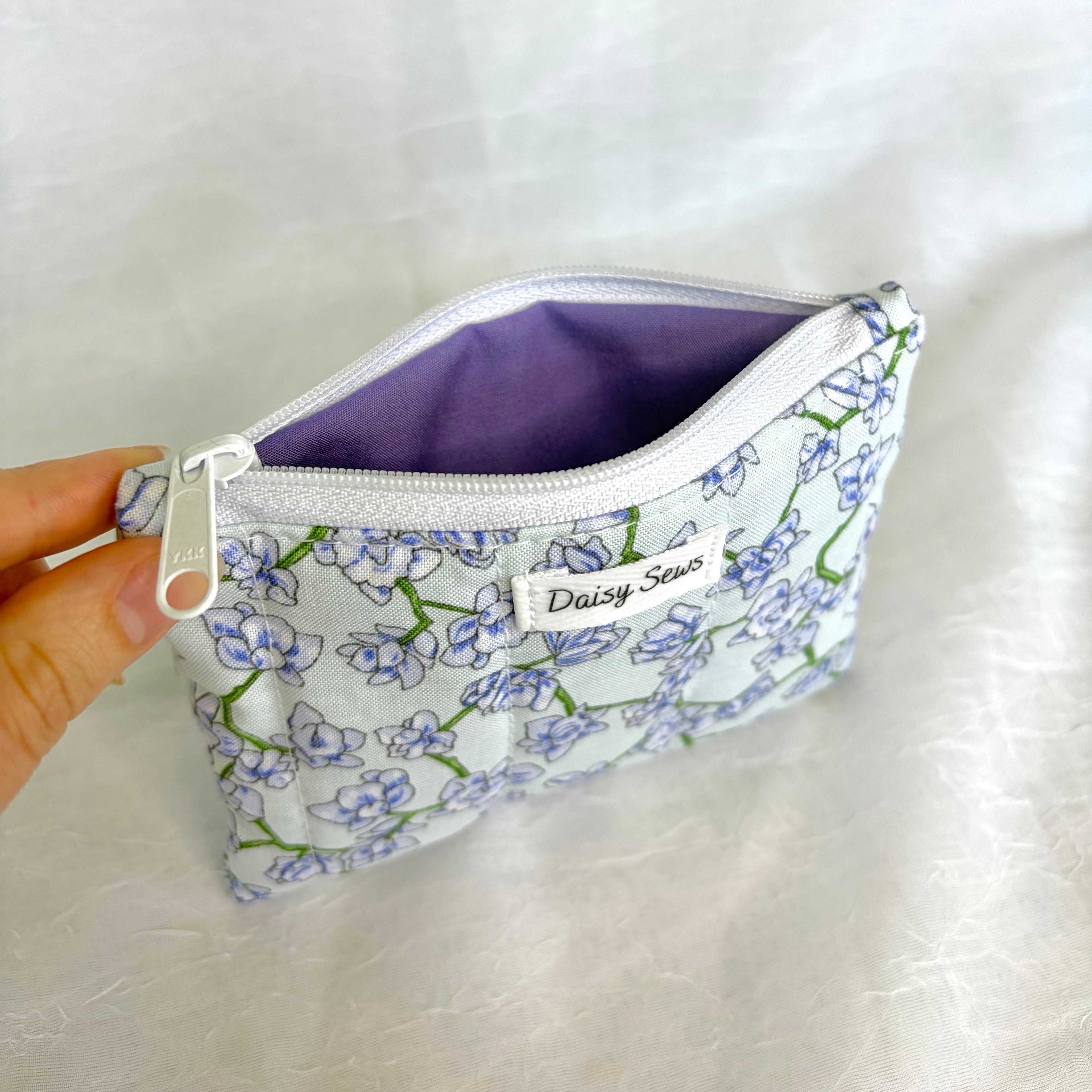 blue Floral-patterned pouch with a purple interior held by a hand on a white background
