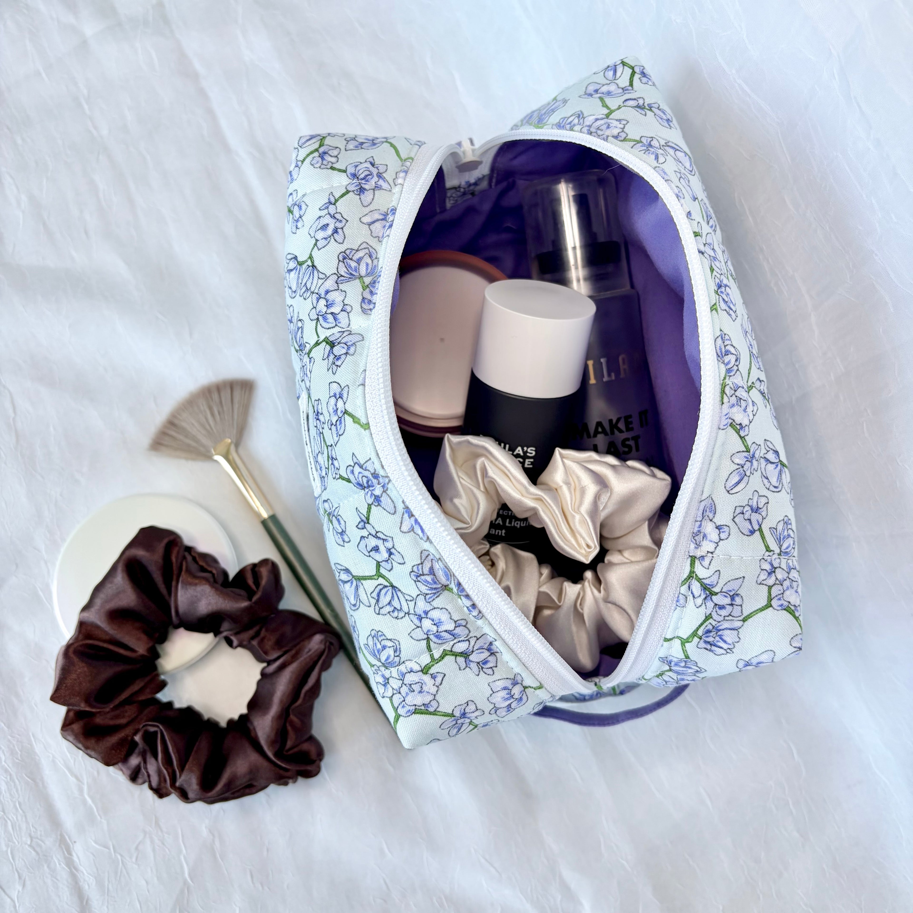Open floral-patterned makeup bag with cosmetic items on a white surface