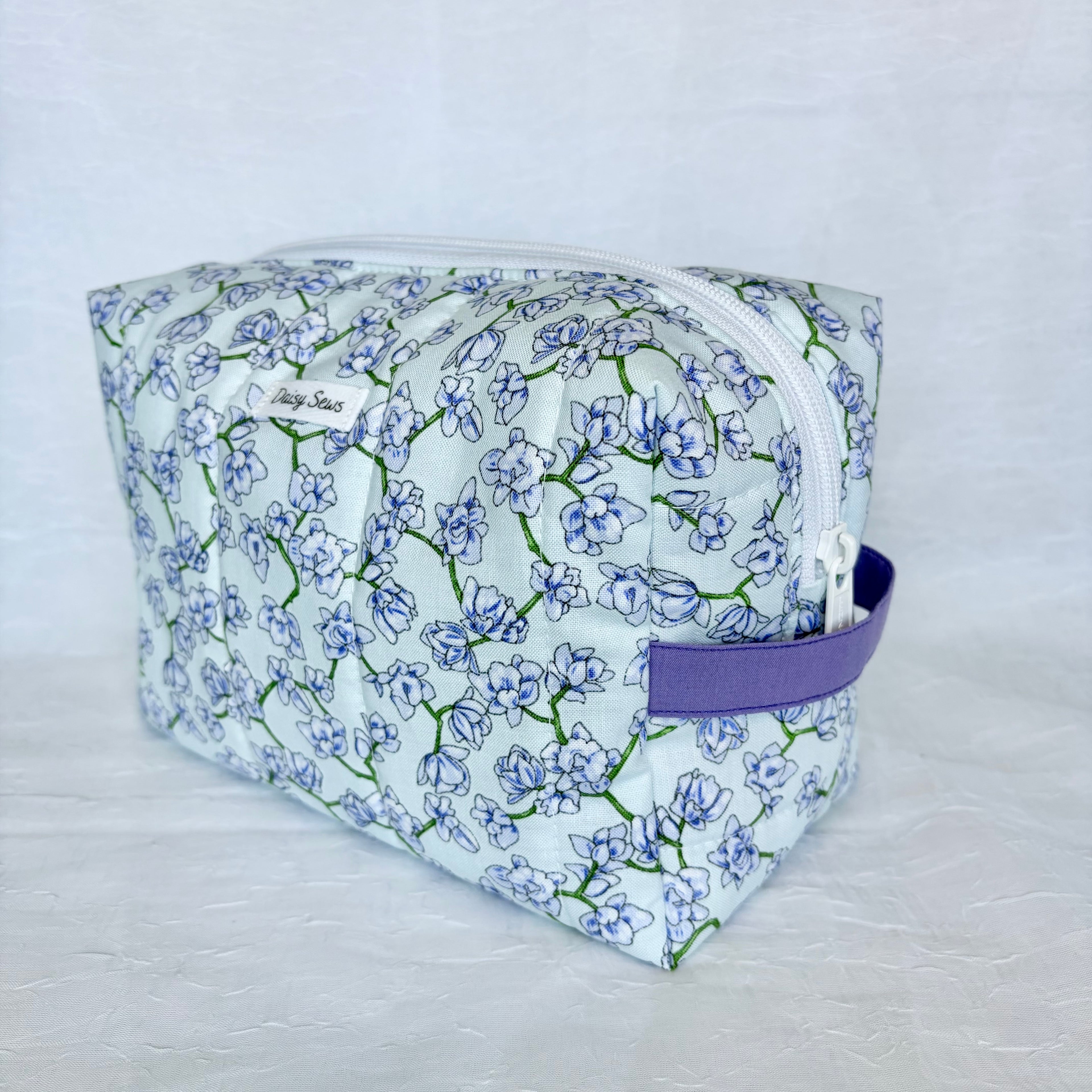 light blue Floral-patterned toiletry bag with a purple strap on a light gray background