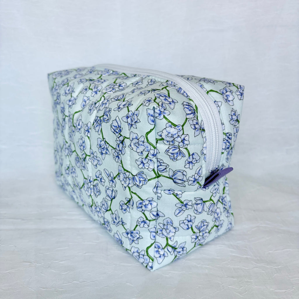 Floral-patterned pouch with a white zipper and purple tab on a light gray background