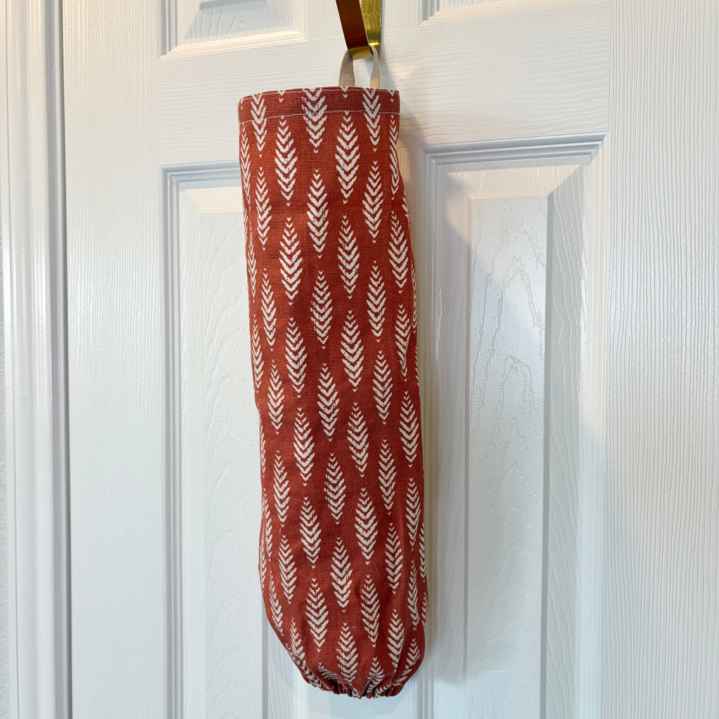 Orange and White Plastic Bag Organizer with a tan loop hanging on a gold hook against a white door
