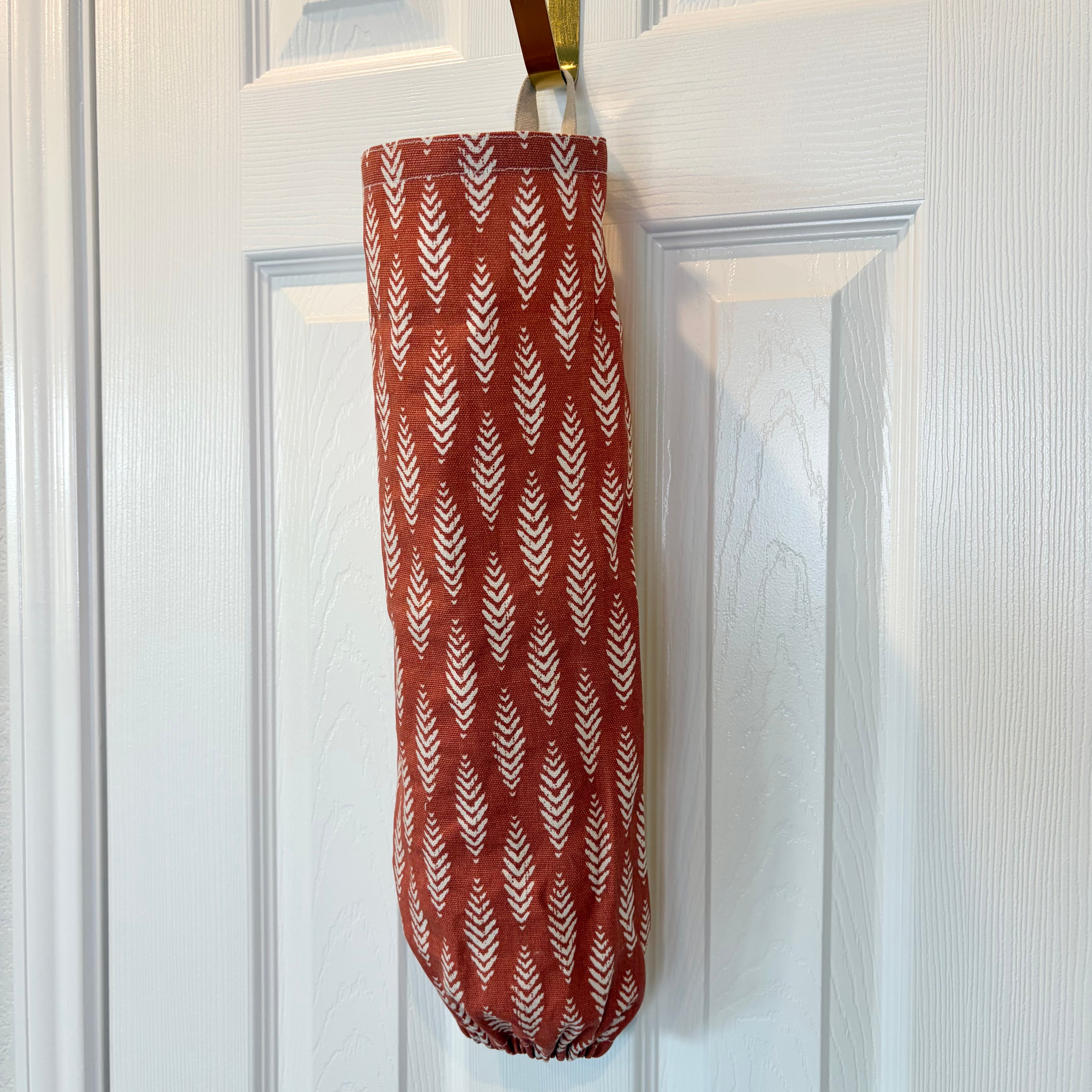 Orange and White Plastic Bag Organizer with a tan loop hanging on a gold hook against a white door