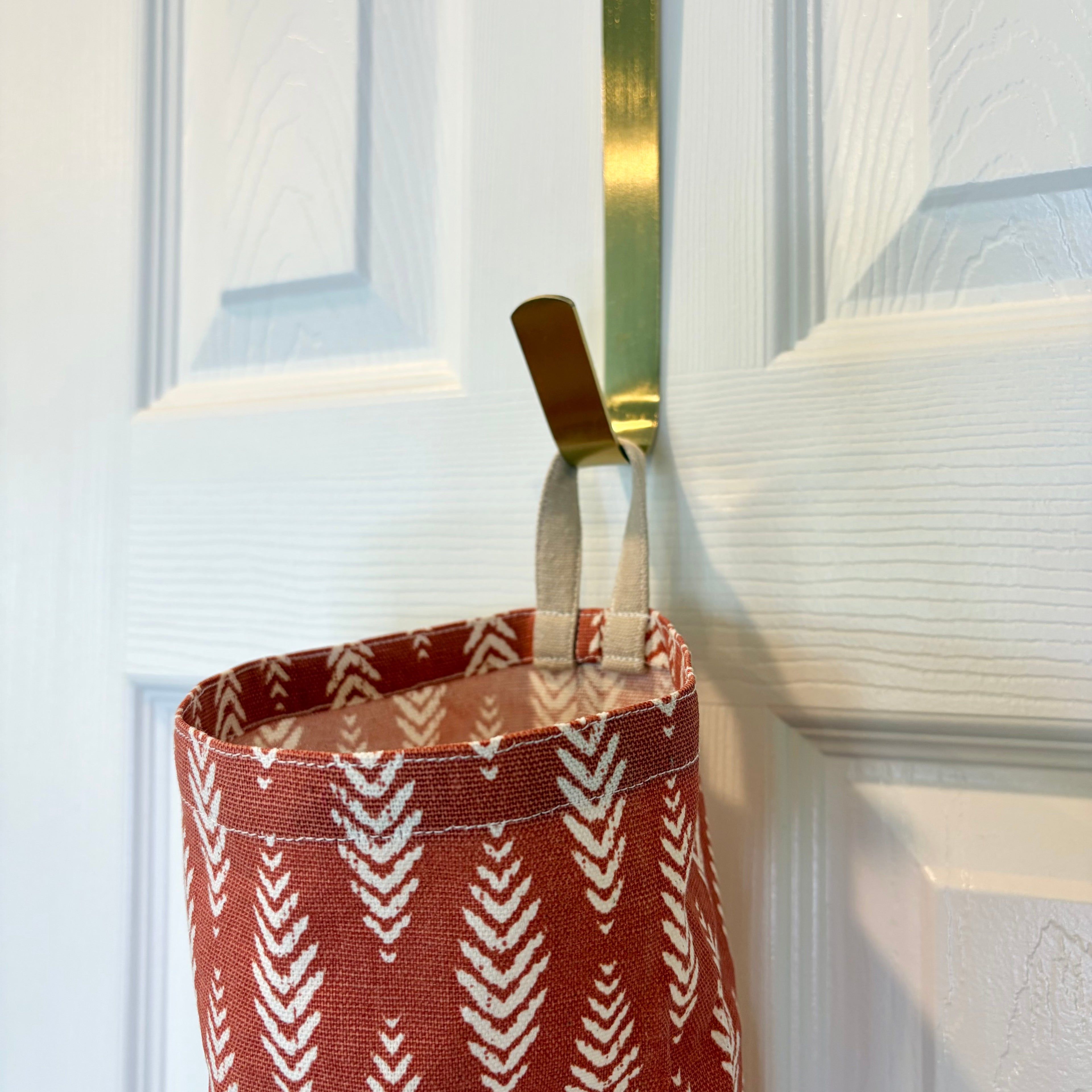 close up of Orange and White Plastic Bag Organizer with a tan loop hanging on a gold hook against a white door