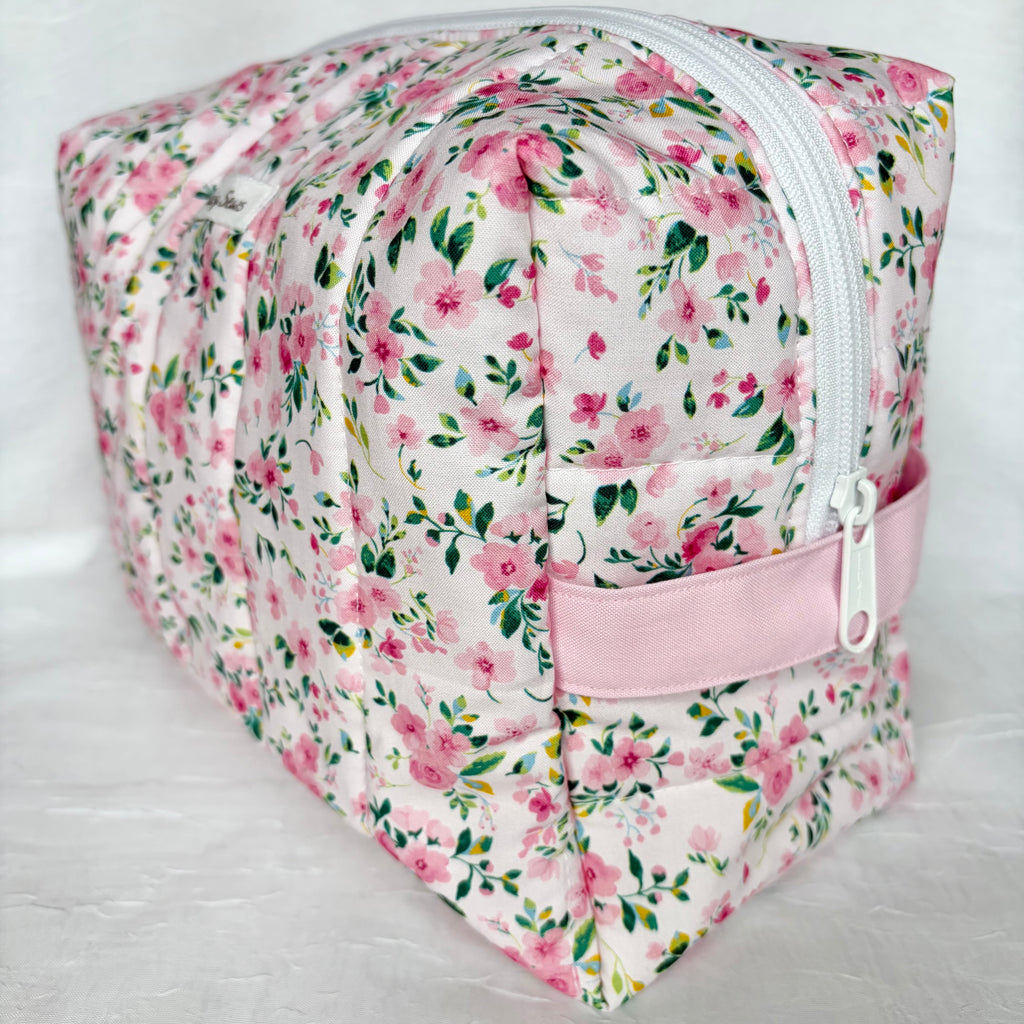 side view of light pink handle and white zipper on pink and green floral boxy bag with white label on white background