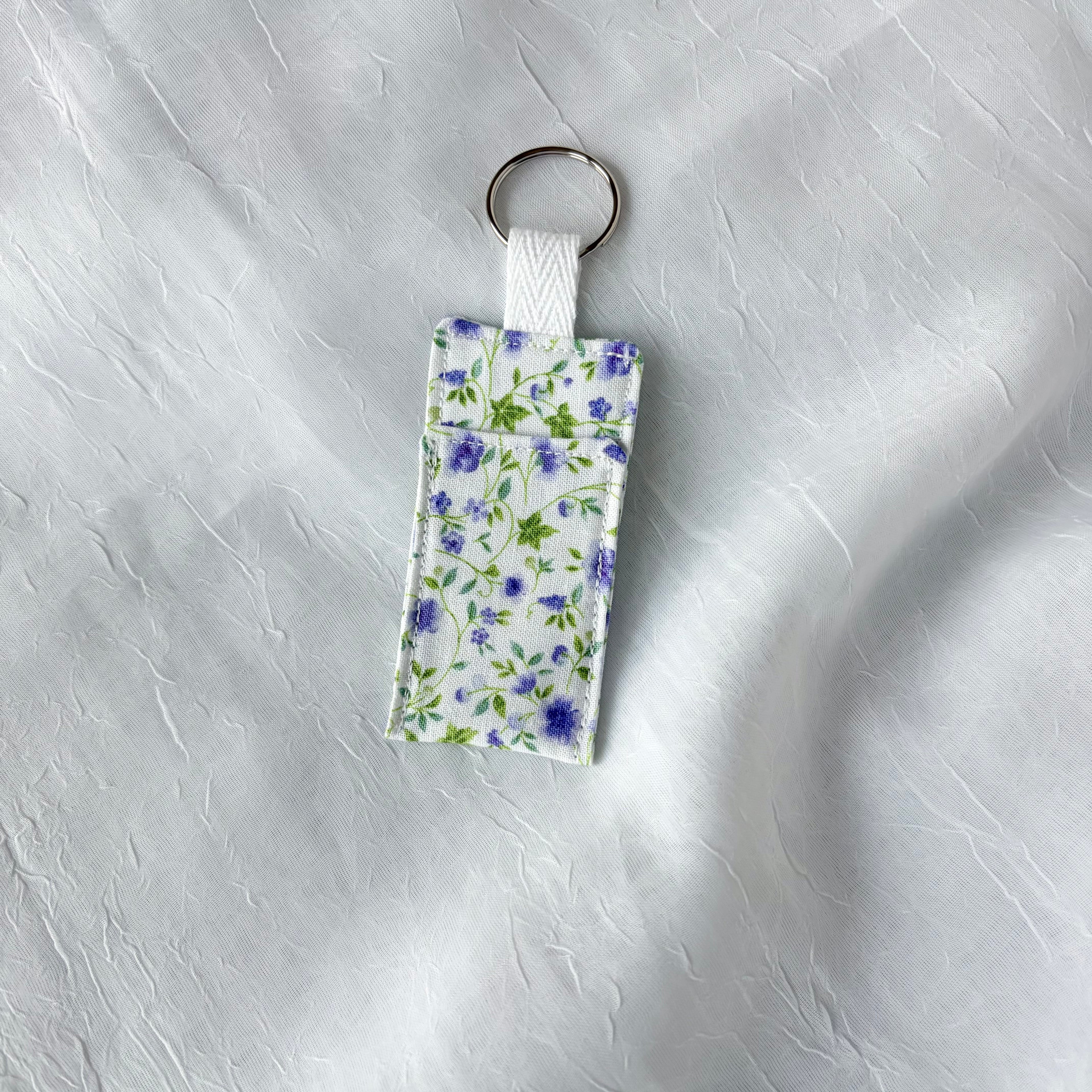 Purple floral with green leaf accents chapstick holder with keychain ring on a textured white background