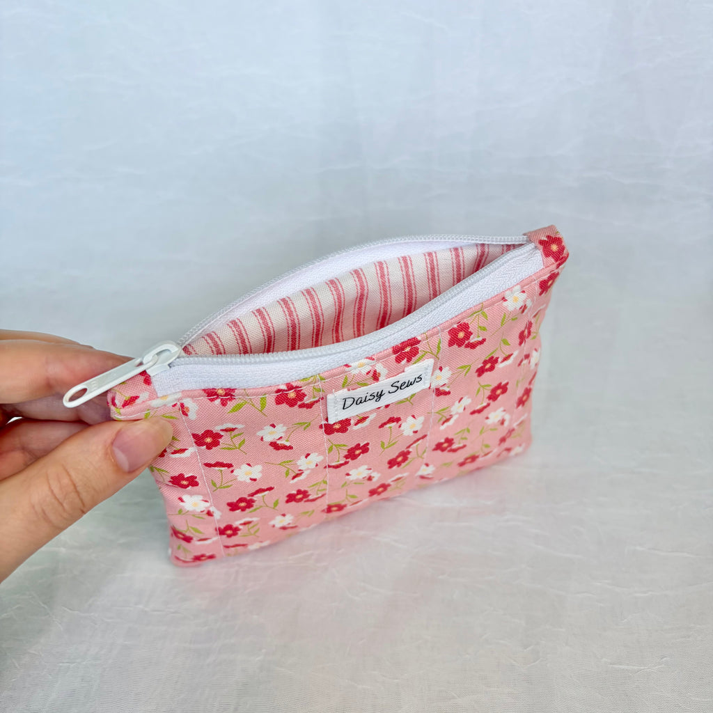 Floral-patterned zipper pouch with pink striped liner held by a hand on a light gray background