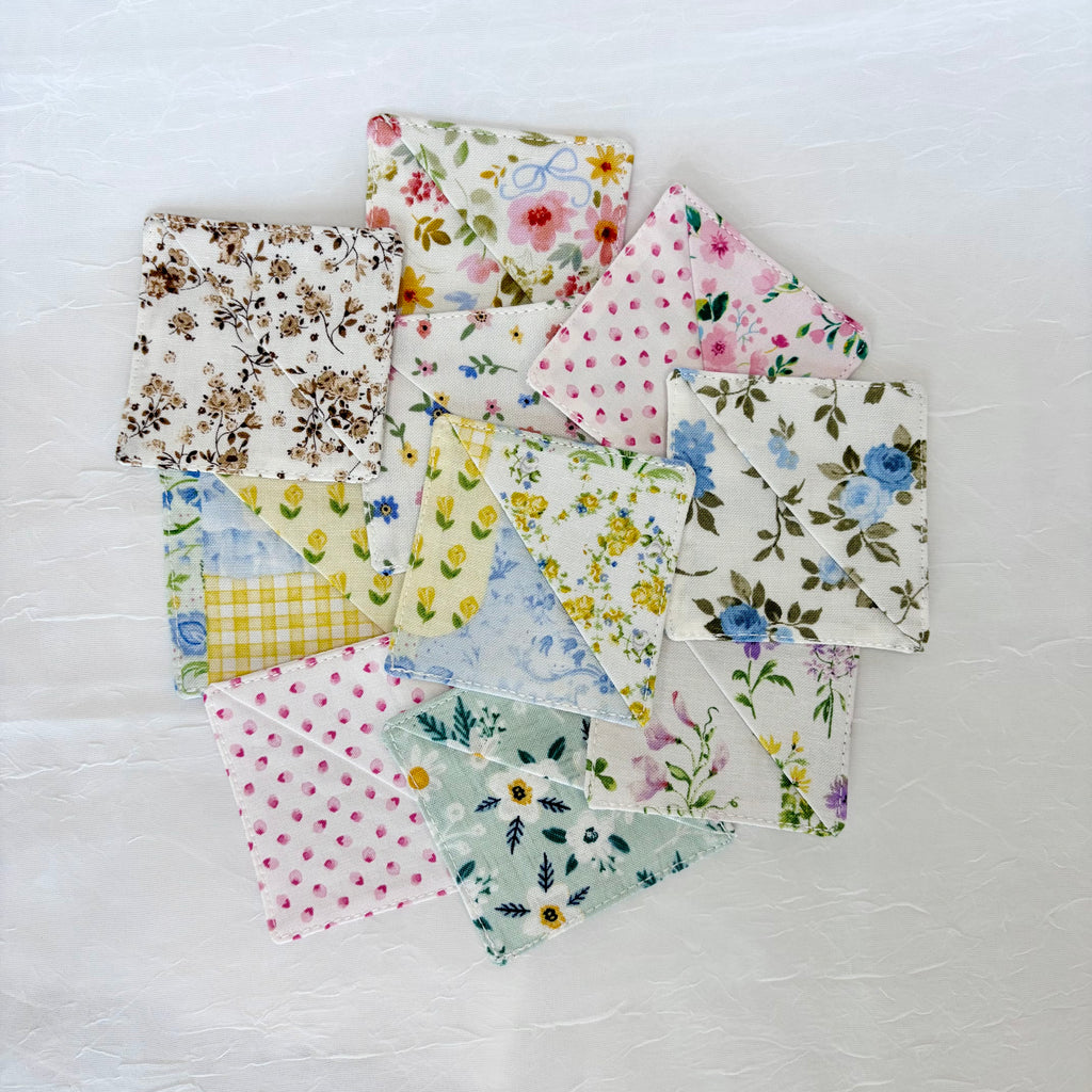 A group of small square fabric bookmarks with assorted floral and polka dot patterns, arranged in a circle on a white textured background.