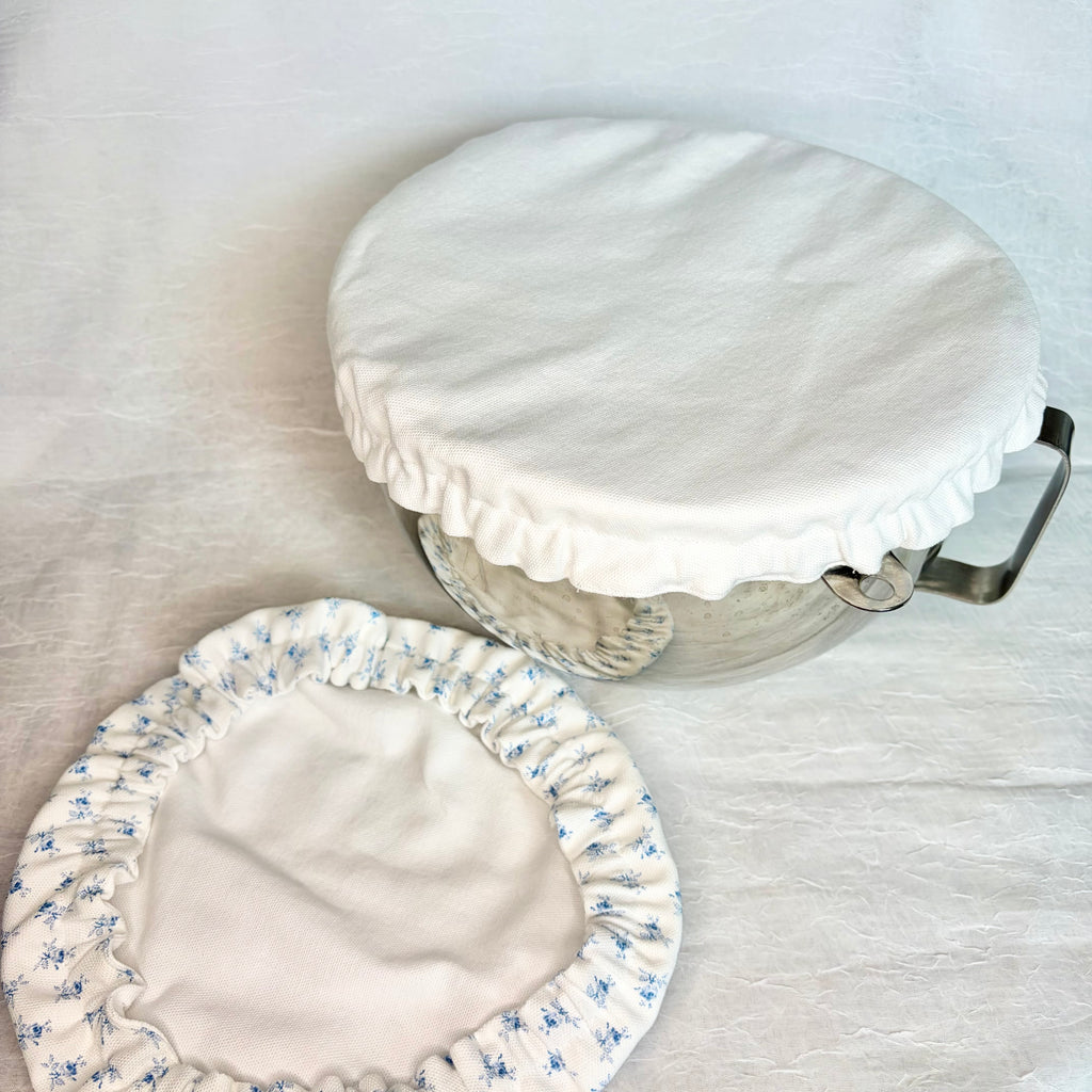 white bowl cover on metal bowl with handle and same bowl cover on surface showing white on the second side and blue flowers on the other side