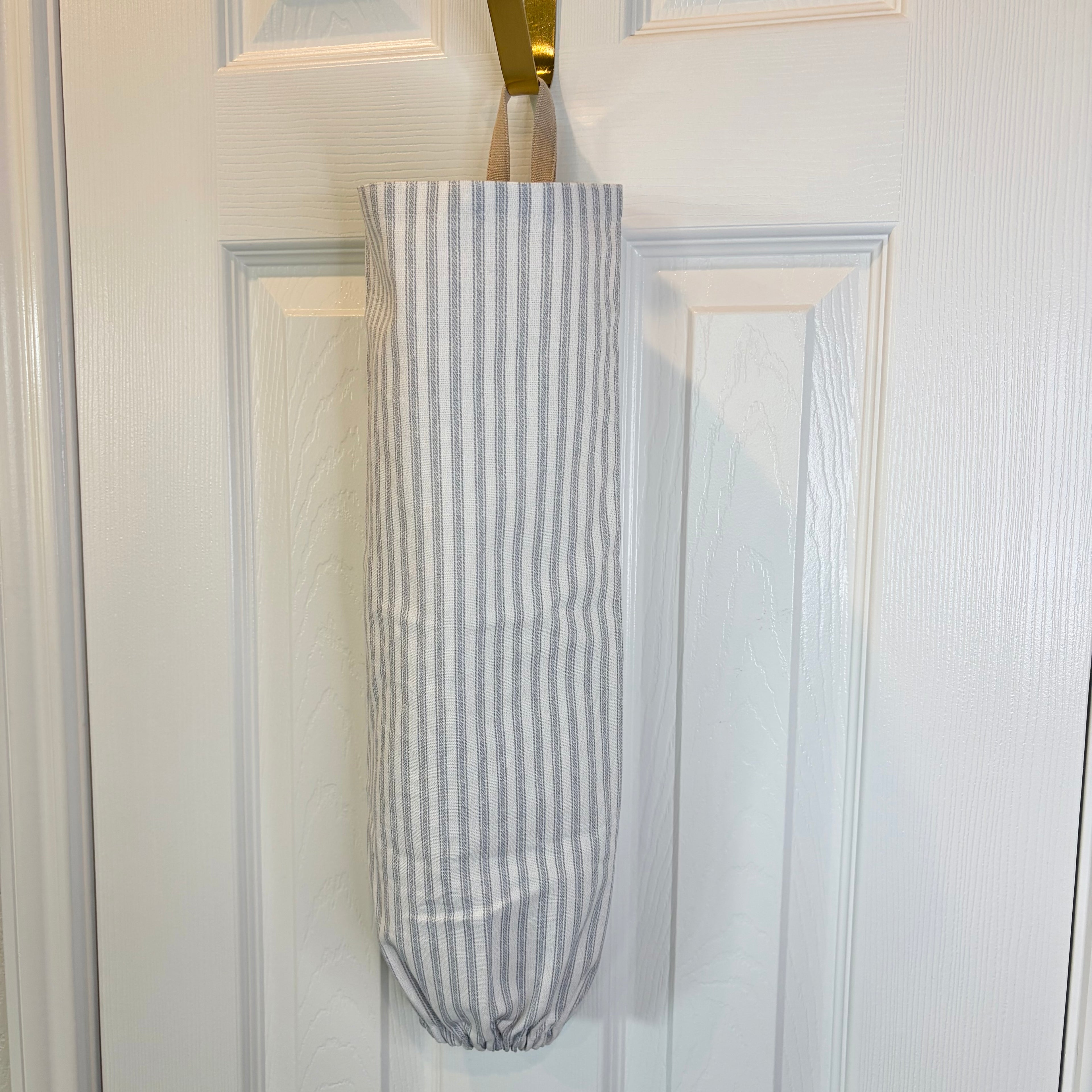White and Blue striped Plastic Bag Organizer with tan loop hanging on a gold hook against a white door