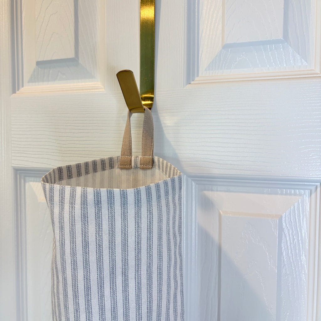 close up of tan loop on White and Blue striped Plastic Bag Organizer hanging on a gold hook against a white door