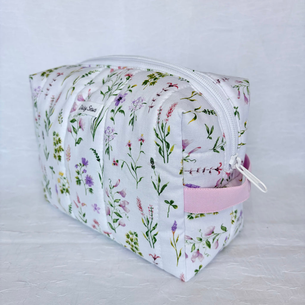 Floral-patterned cosmetic bag with a white zipper and pink handle on a light gray background