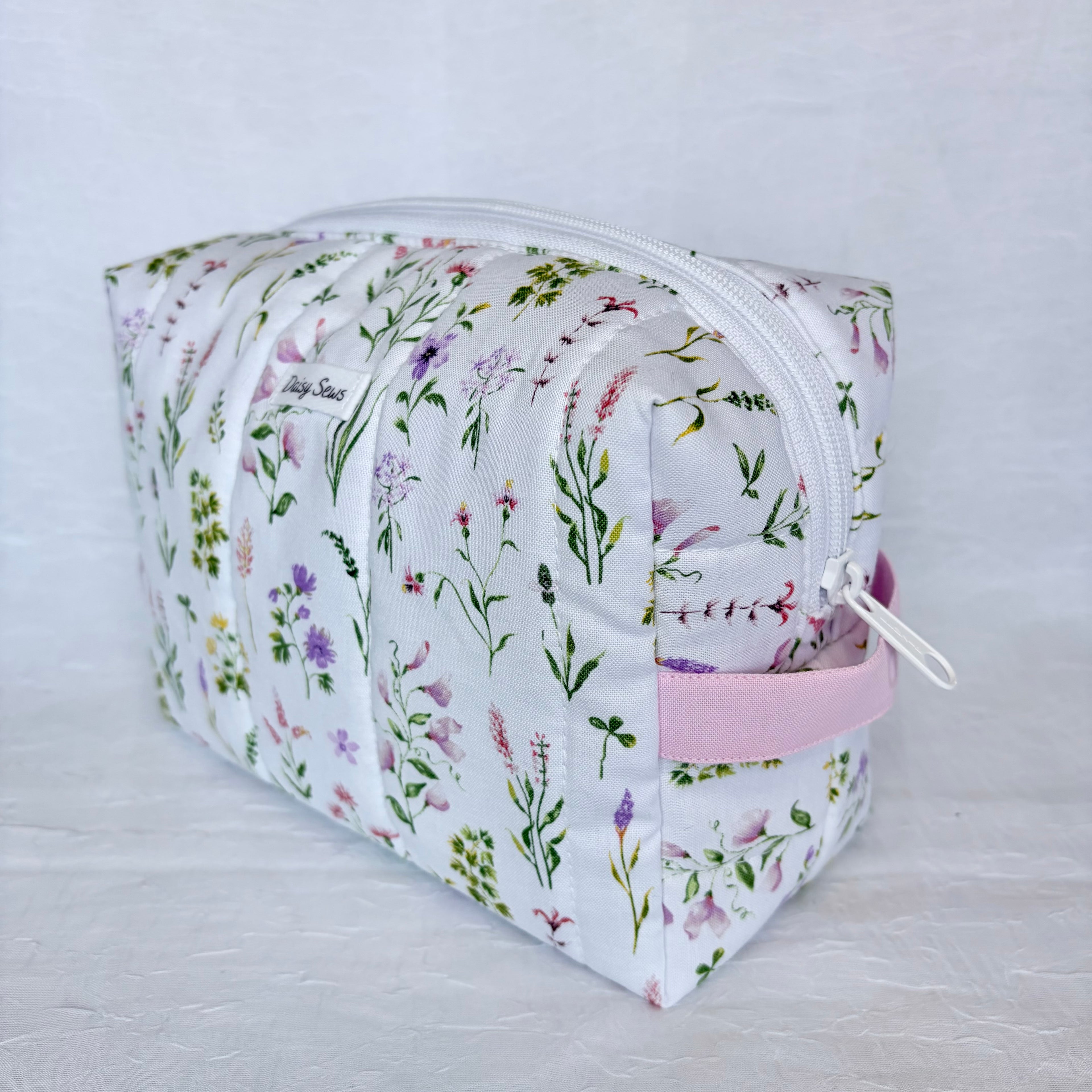 Floral-patterned cosmetic bag with a white zipper and pink handle on a light gray background