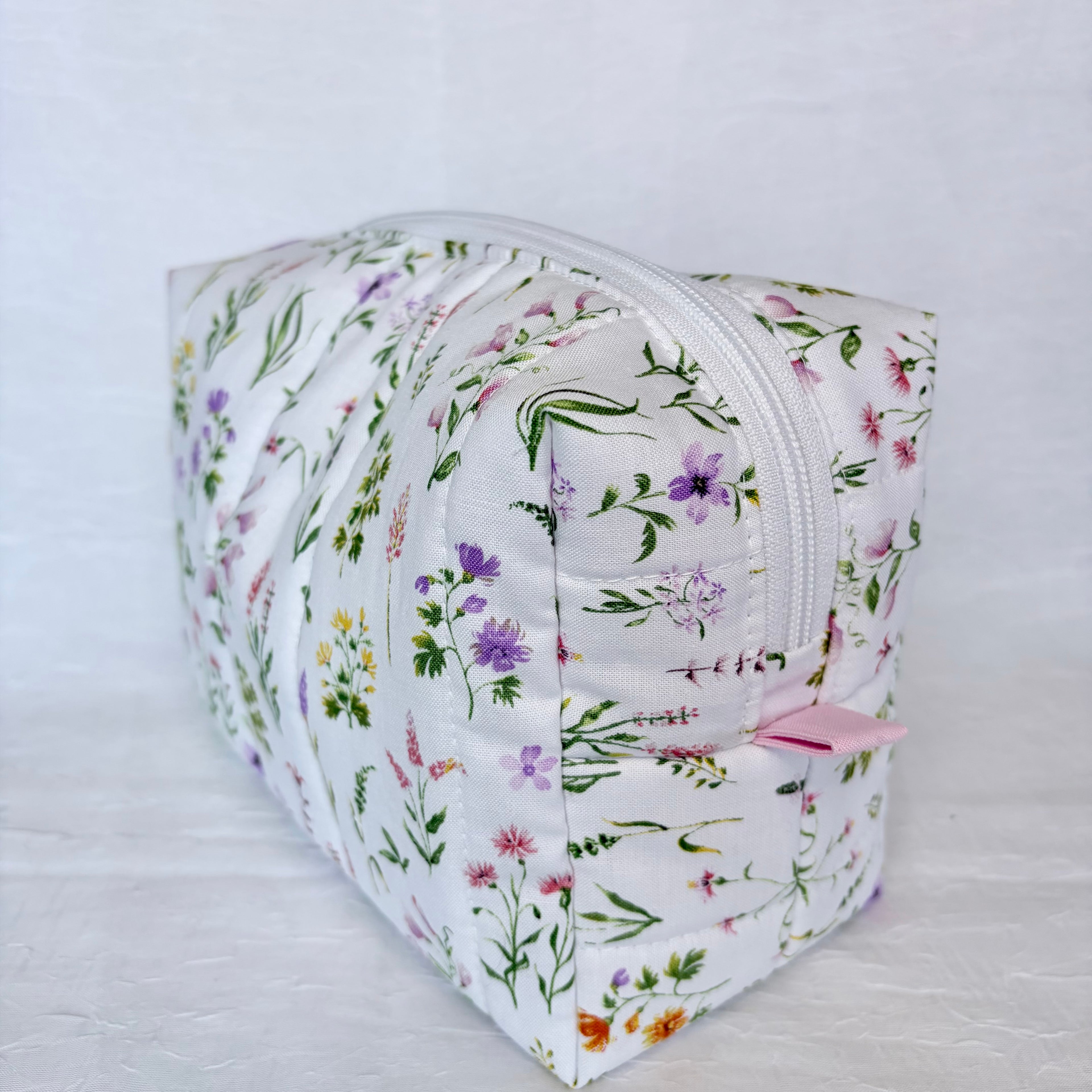 Floral-patterned cosmetic bag with pink tab on a light gray background