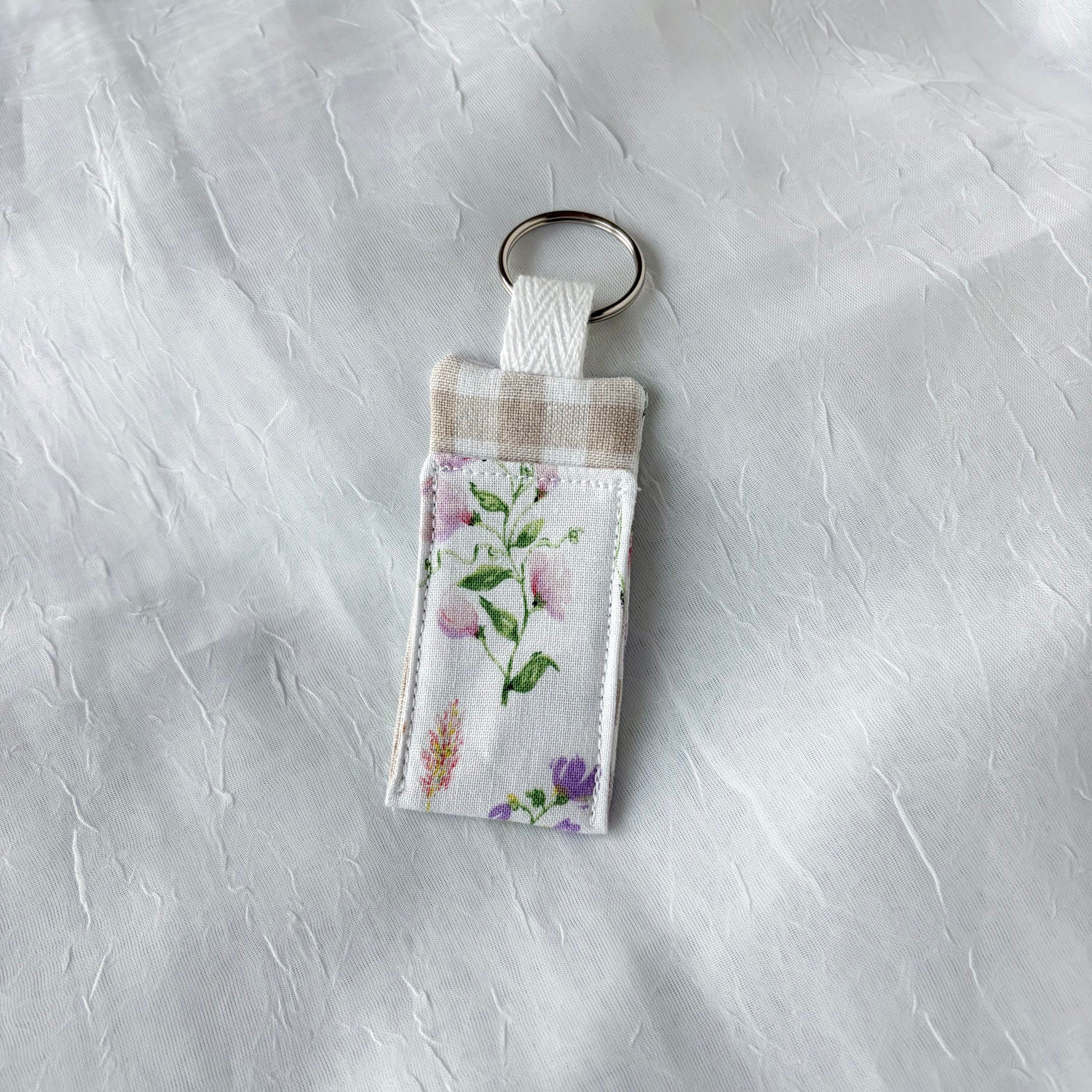 Floral with beige gingham accent chapstick holder with keychain ring on a textured white background