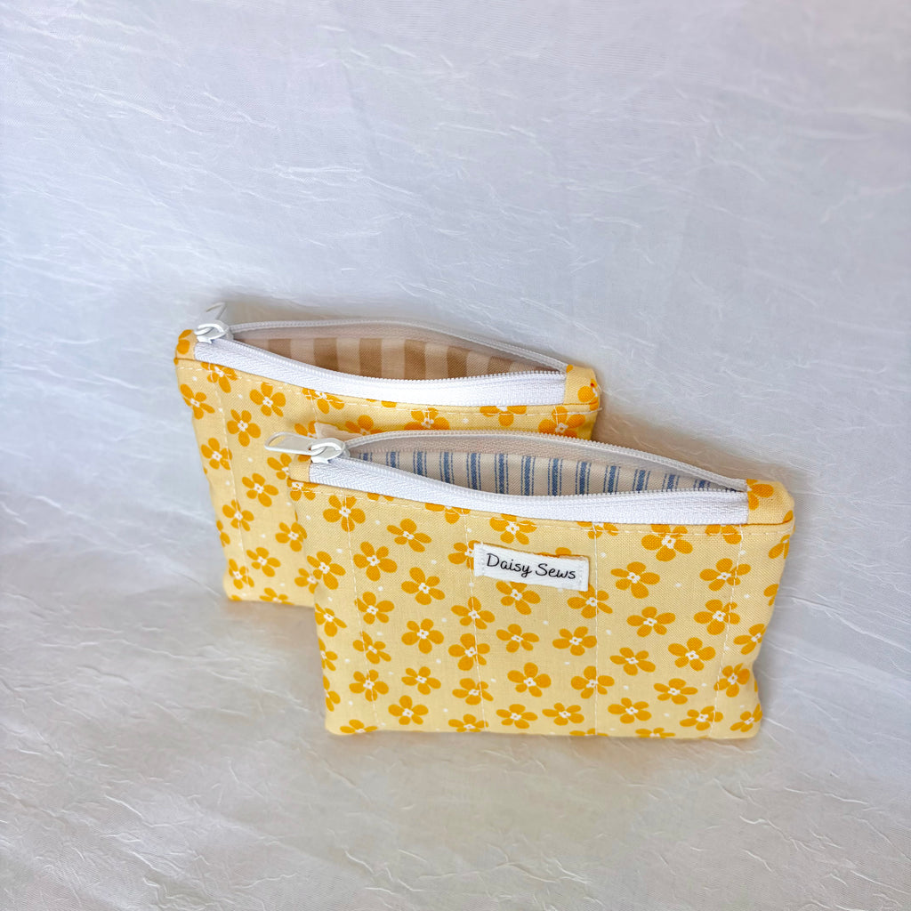 Two yellow floral pouches with white zippers on a light gray background. liners are tan stripes on the left and blue stripes on the right