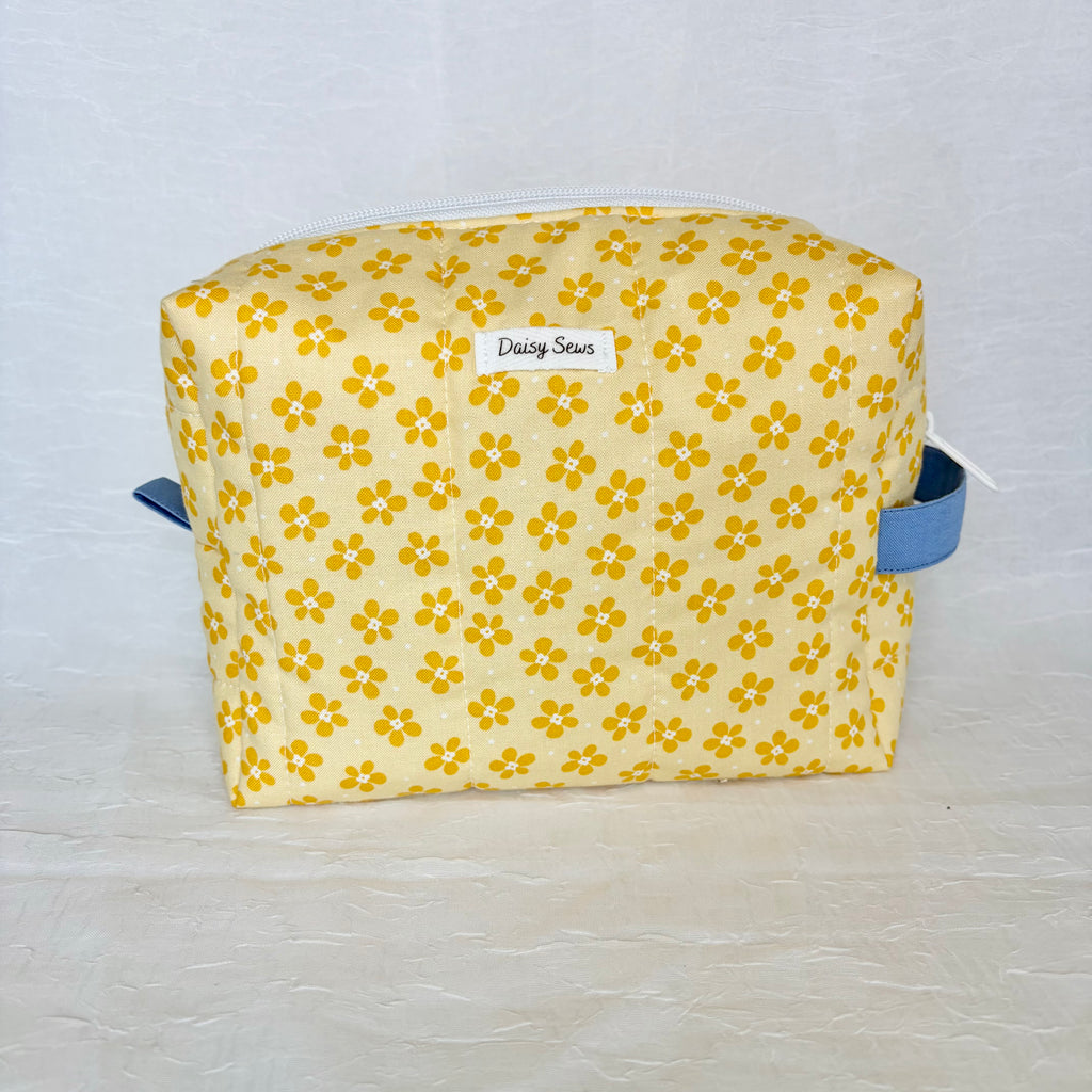 Yellow floral-patterned bag with blue straps on a light gray background