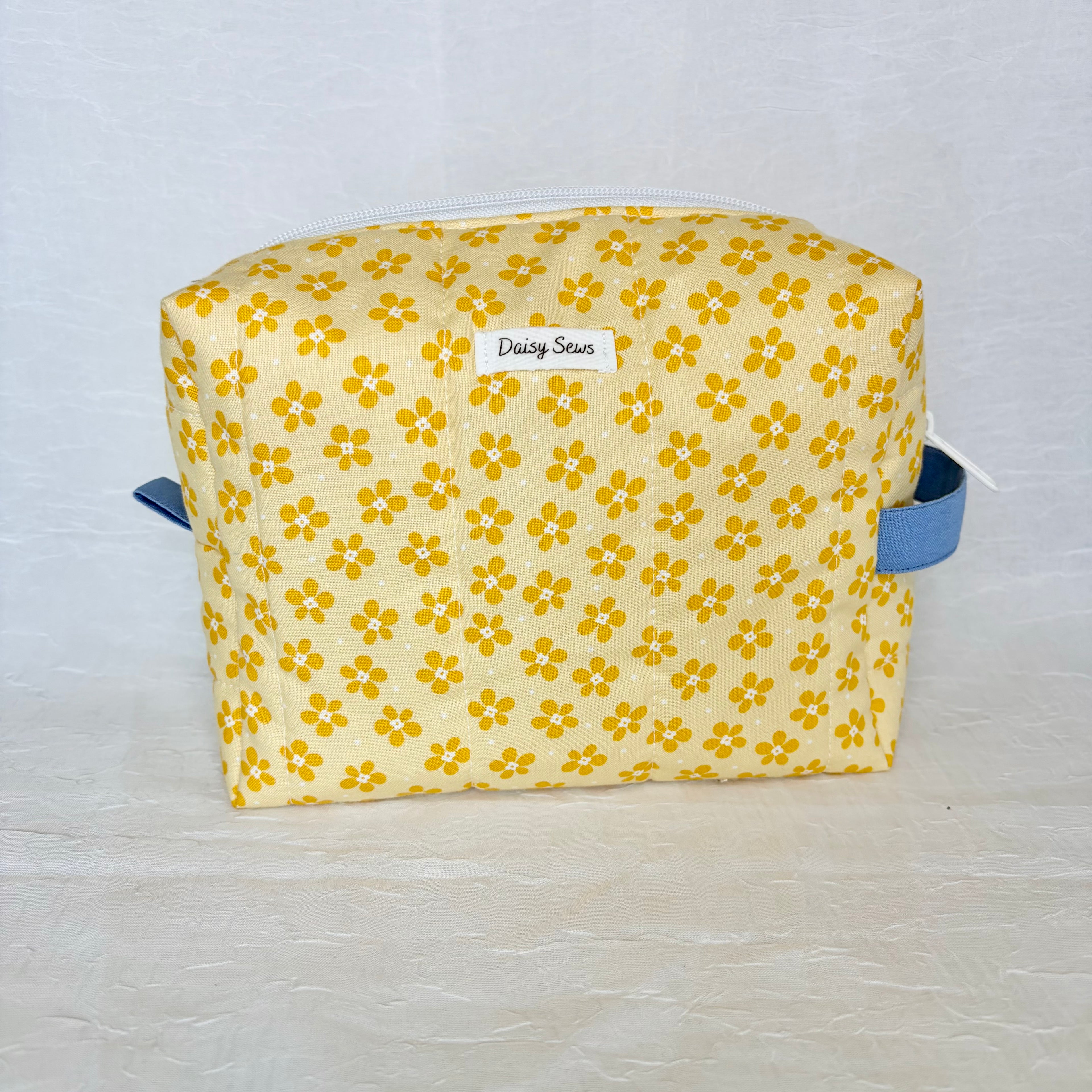 Yellow floral-patterned bag with blue straps on a light gray background