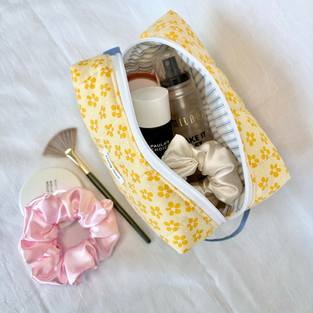 Yellow floral makeup bag with cosmetic items on a white surface