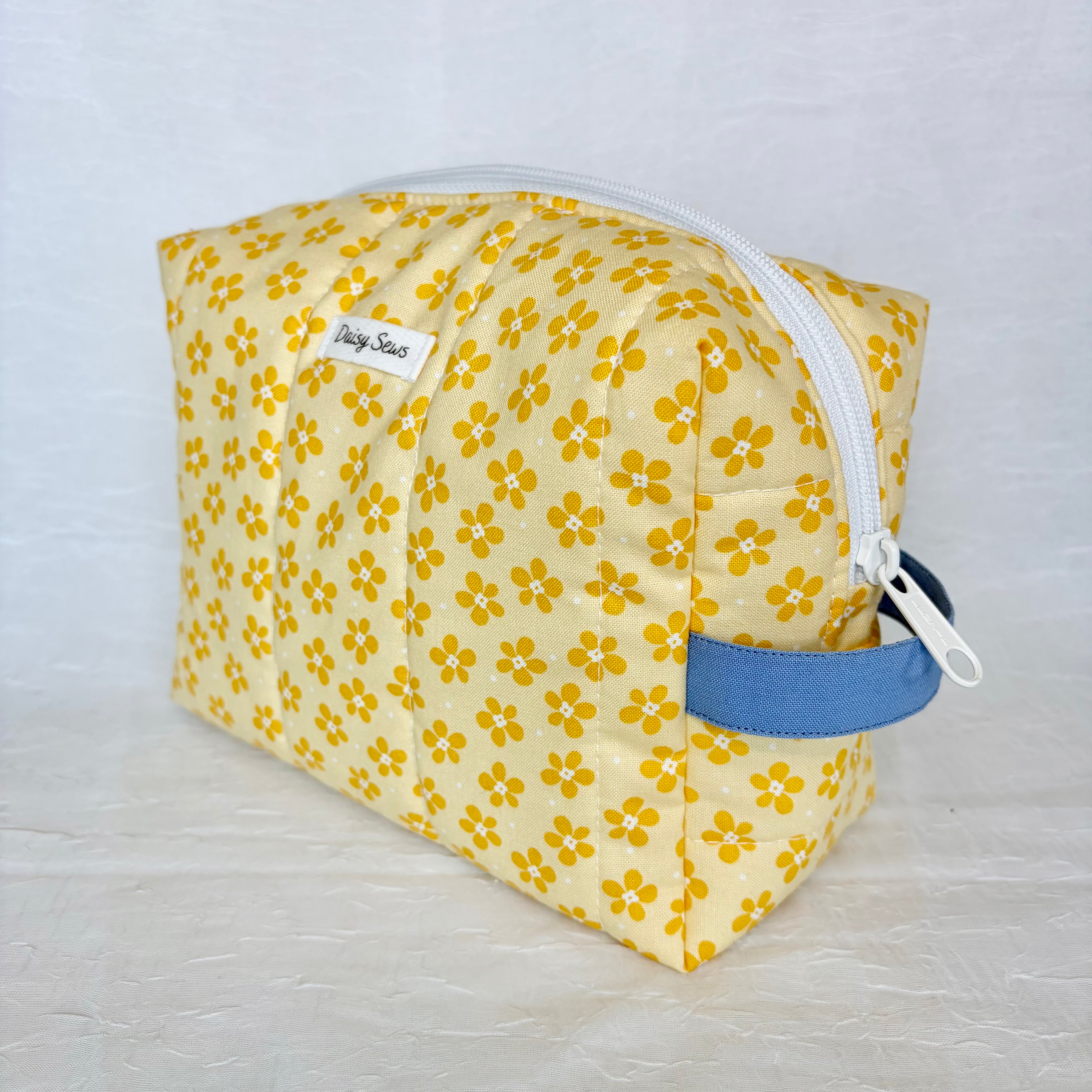 Yellow floral-patterned pouch with a blue handle on a light gray background