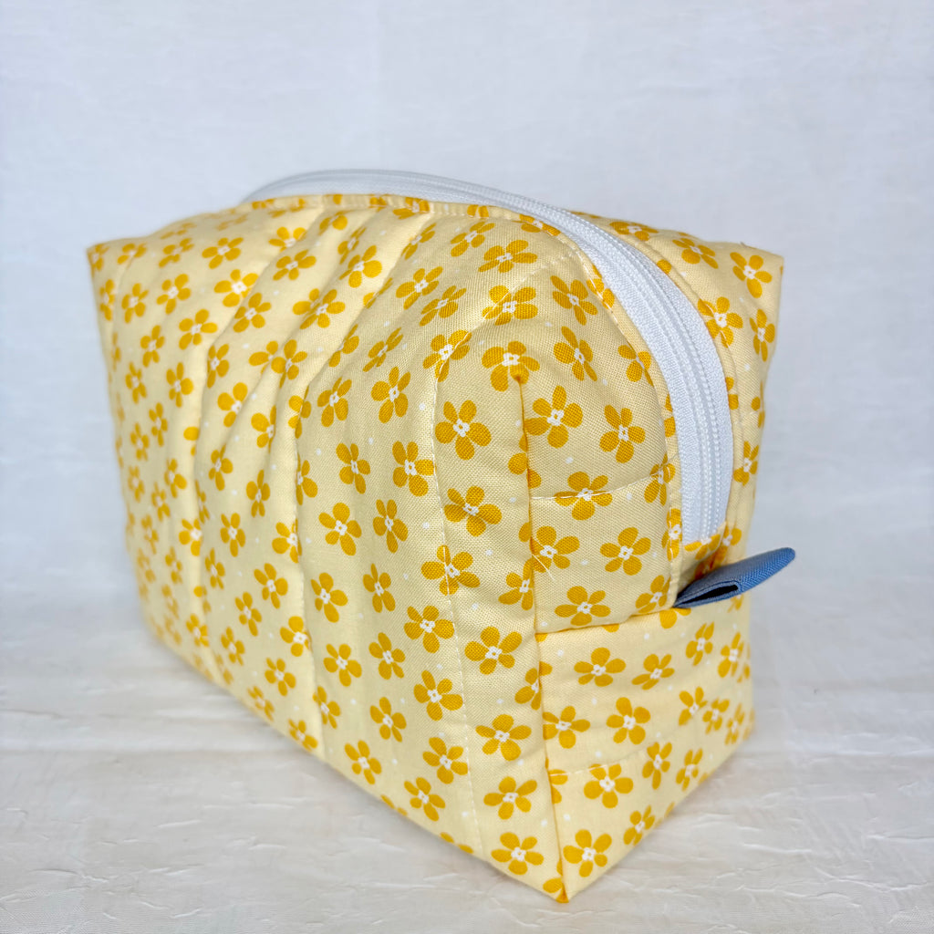 Yellow floral-patterned fabric bag with a white zipper and blue tab on a light gray background