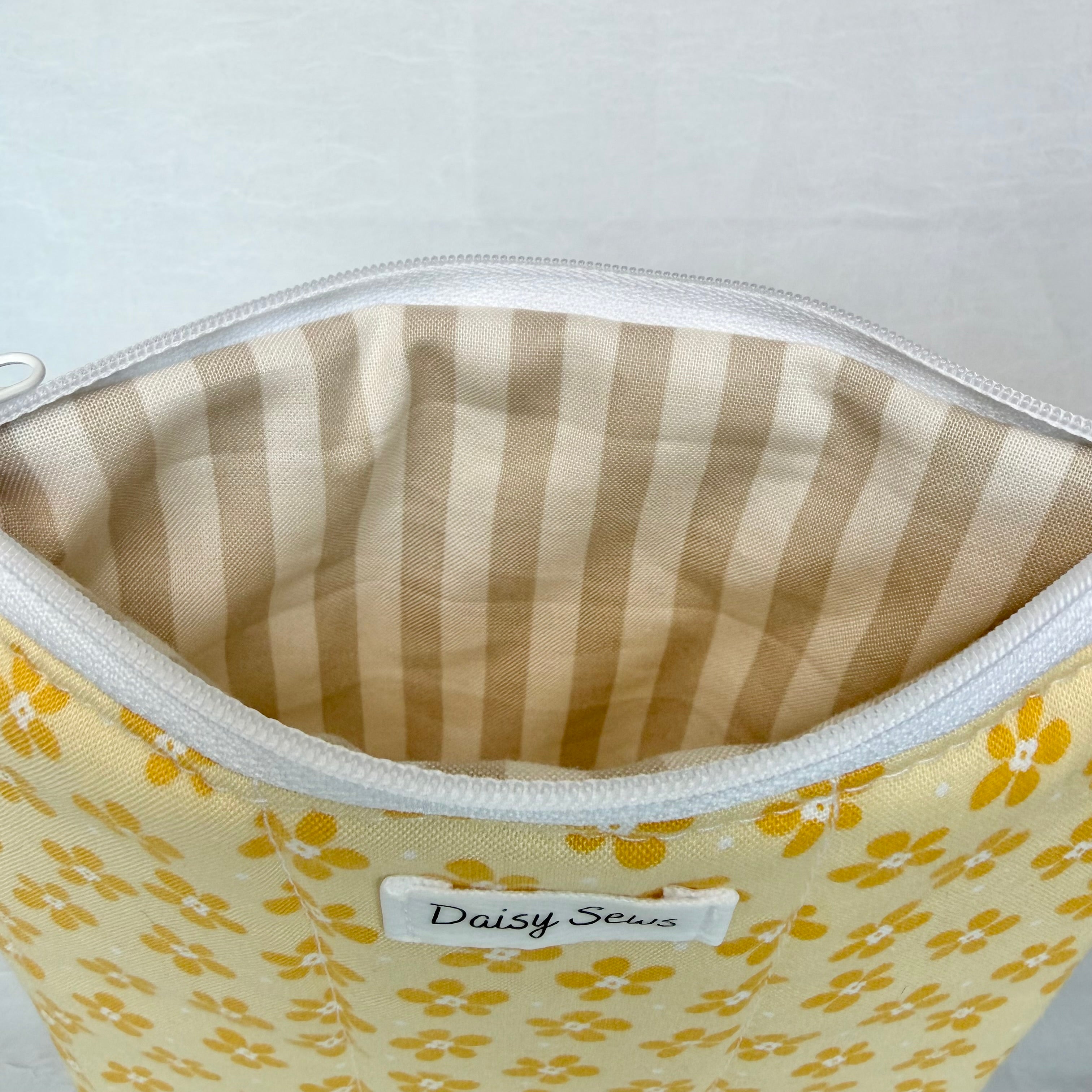 Fabric pouch with yellow floral pattern and tan striped lining, featuring 'Daisy Sews' label.