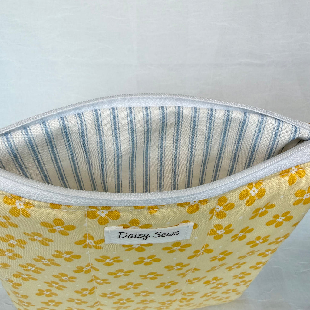 Fabric pouch with yellow floral pattern and blue striped lining, featuring 'Daisy Sews' label.